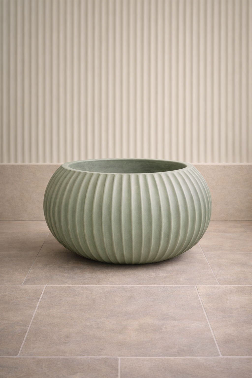 Large round ceramic planter with vertical ribbing, placed on a tiled floor against a textured beige wall.