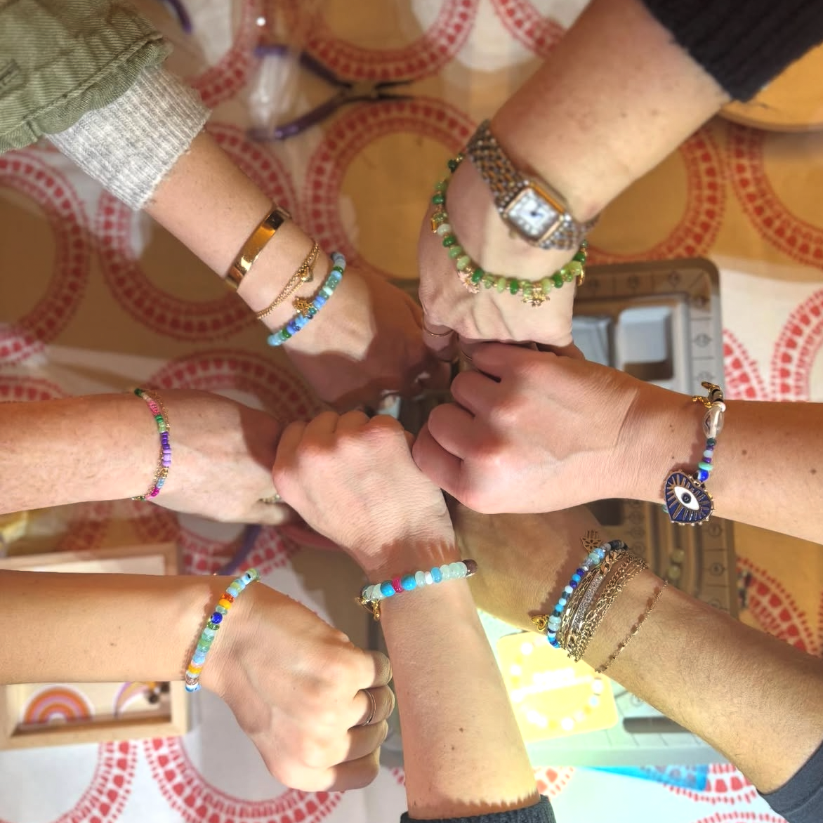 Multiple hands with different jewelry, including bracelets and rings, joining together in a display of unity over a table with a patterned tablecloth.