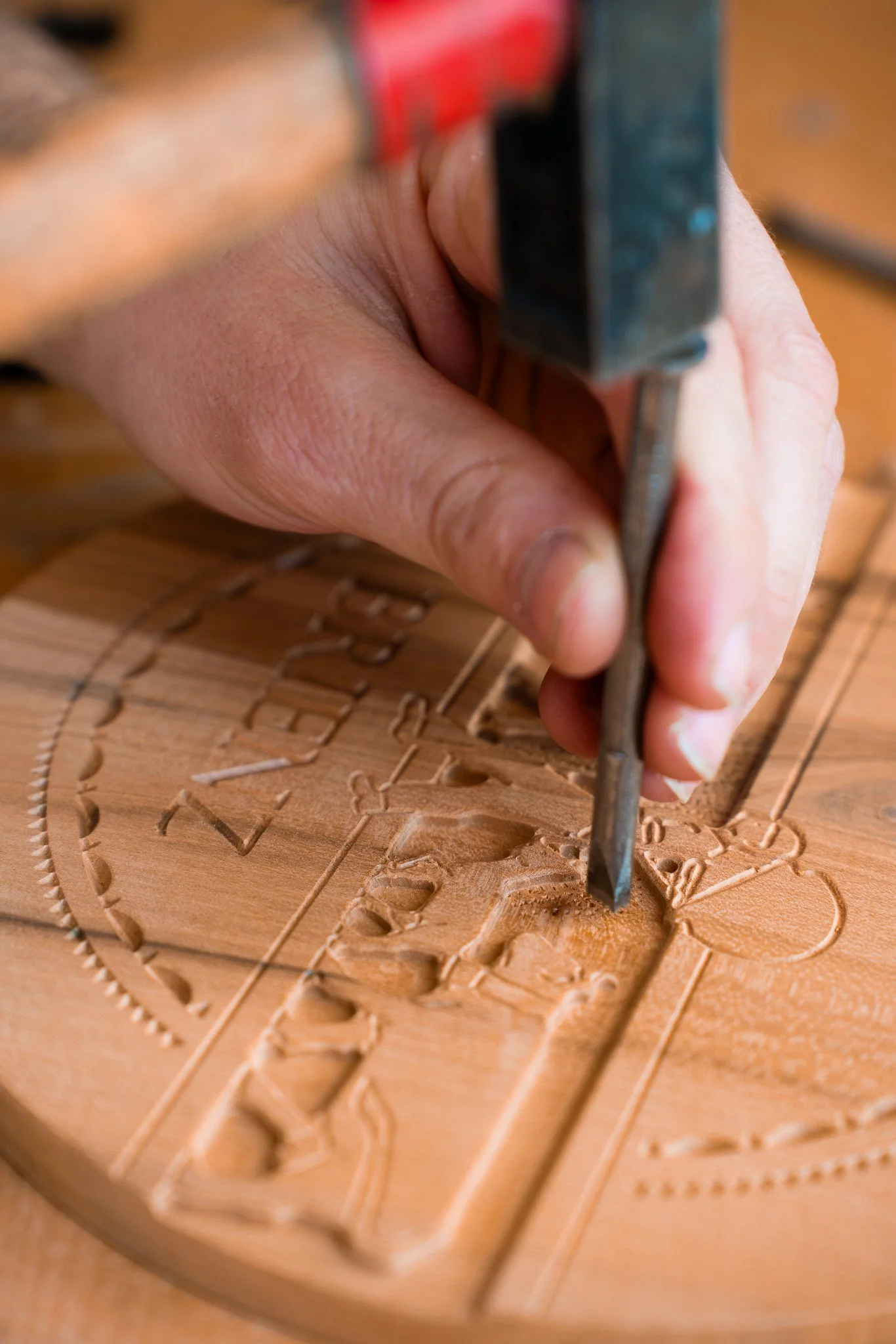 Hand, die in Holz arbeitet, auf dem eine geschnitzte Karte oder ein Holzrelief zu sehen ist, mit einer Art Meißel, um Details herauszuarbeiten.