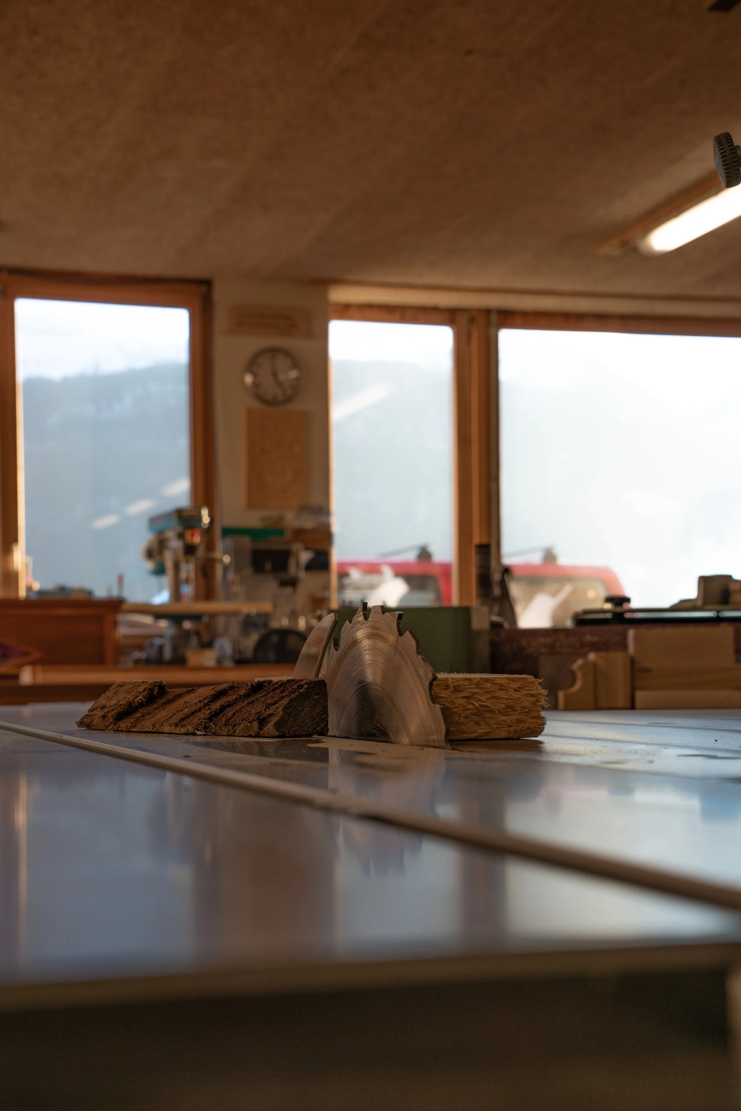 Ein Frästisch mit einer rotierenden Kreissäge in einer Werkstatt, im Hintergrund Fenster mit Blick auf Berge.