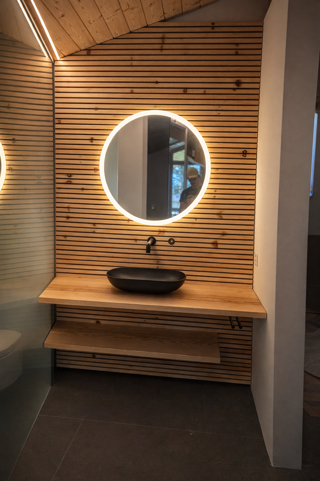 Moderner Waschtisch mit schwarzen Waschbecken, Holzvertäfelung mit beleuchtetem Spiegel im Badezimmer.