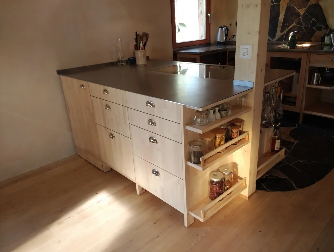 Holzküche mit weißen Schränken, dunklem Küchenblock und offenem Regal mit Gläsern und Gewürzen.