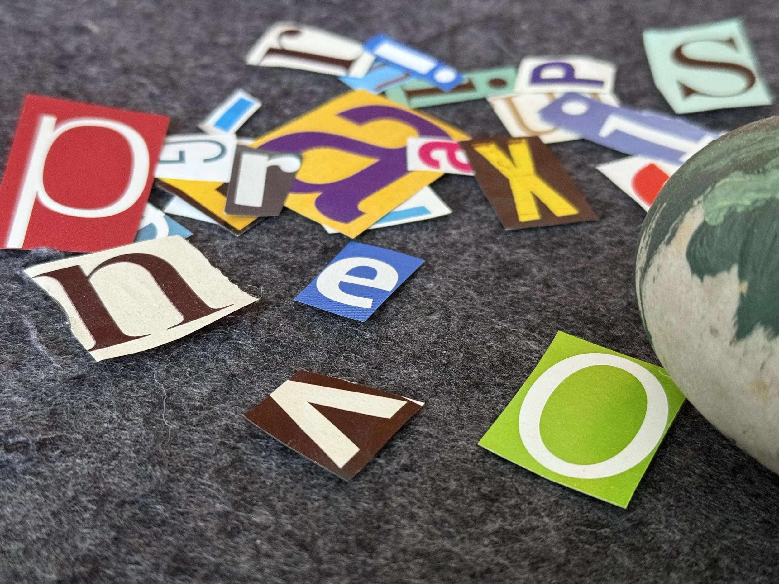 Colorful paper cut-out letters scattered on a dark textured surface with part of a decorative globe visible on the right.