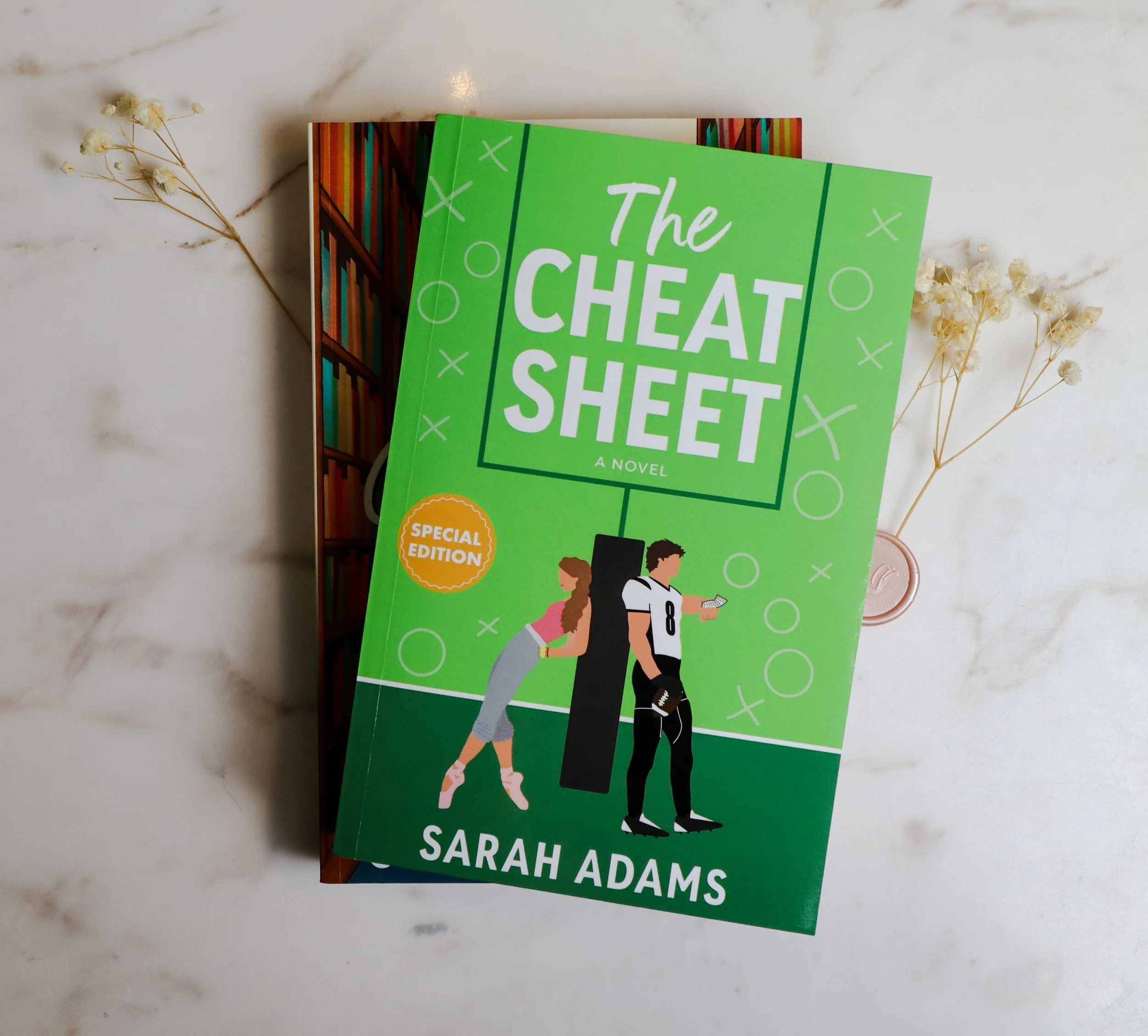 Cover of the book titled 'The Cheat Sheet' by Sarah Adams, featuring an illustration of a girl in ballet clothes leaning on a cushion and a boy in football attire looking at his phone, against a green background with circles and Xs.