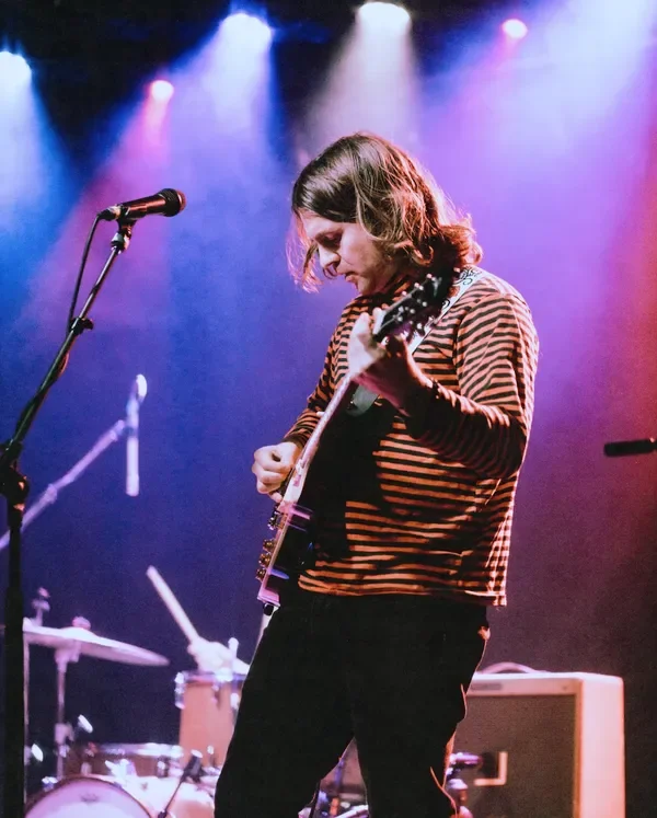 A woman playing an electric guitar on stage with colorful lights shining down.