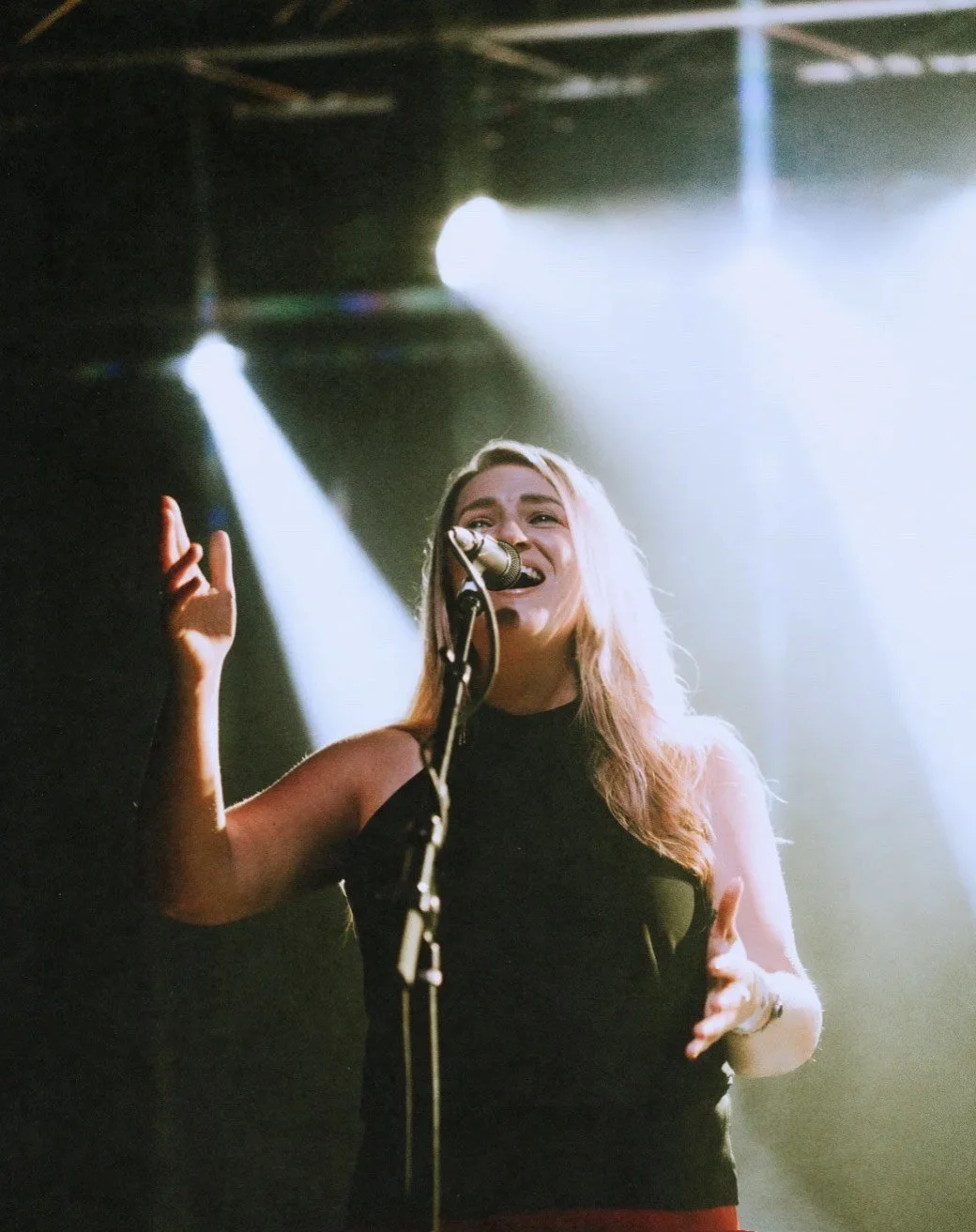 A woman singing into a microphone on stage with bright spotlighting behind her.