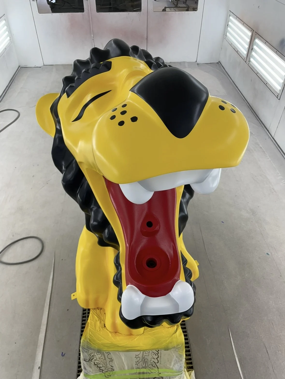 A large, cartoonish sculpture of a lion's head with a yellow face, black mane, and an exaggerated open mouth showing white teeth and a red tongue.