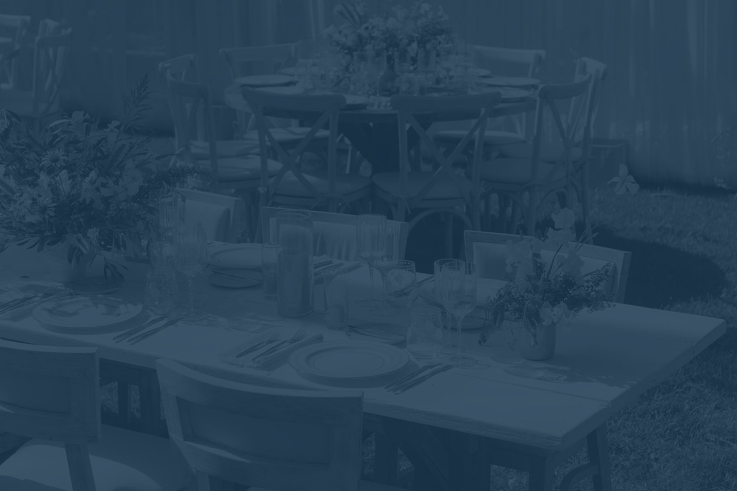 A table set for outdoor dining with plates, glasses, silverware, and floral centerpieces on a garden lawn.