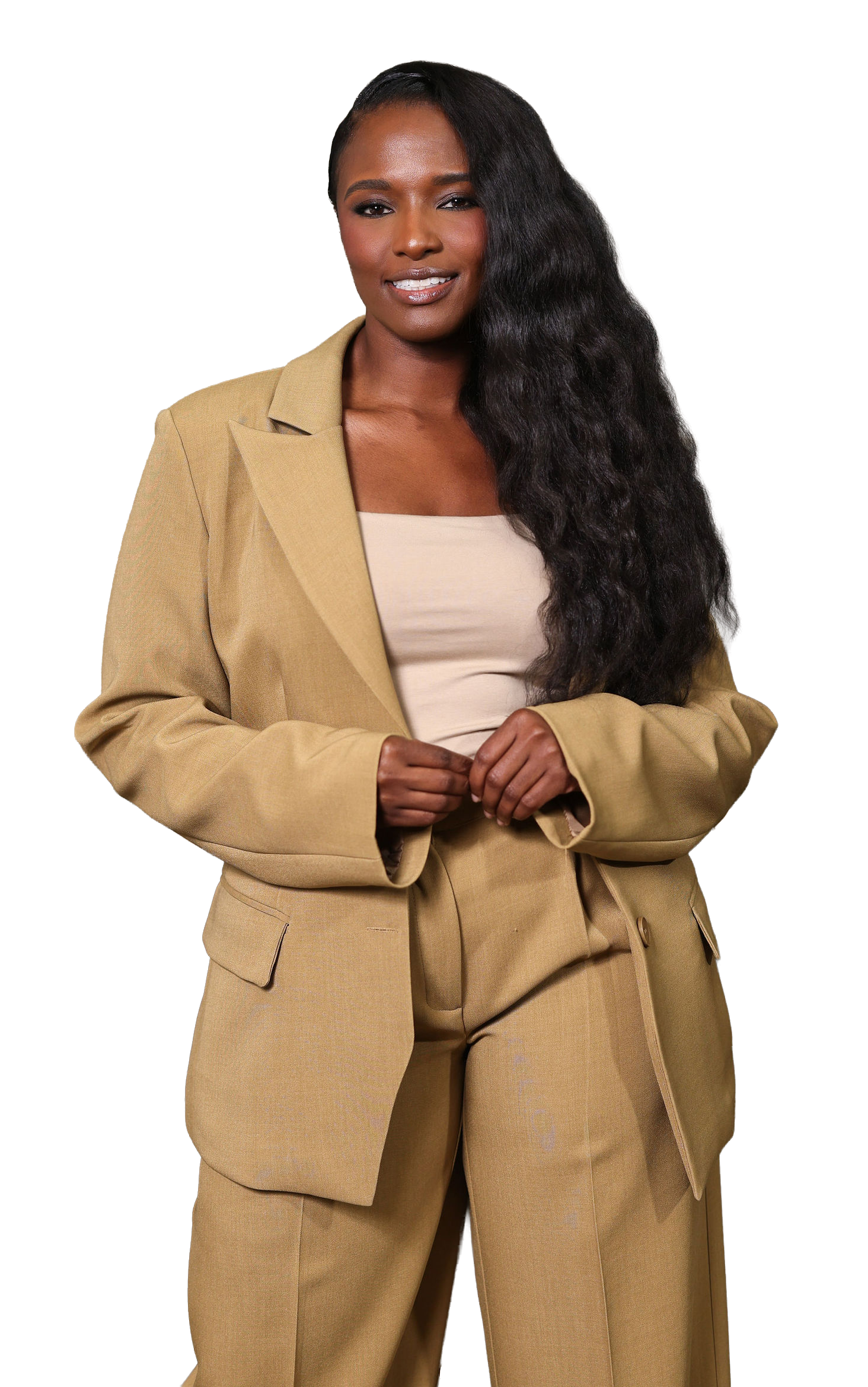 A woman with long, wavy black hair, wearing a beige suit and a beige top, standing against a partial colored background.