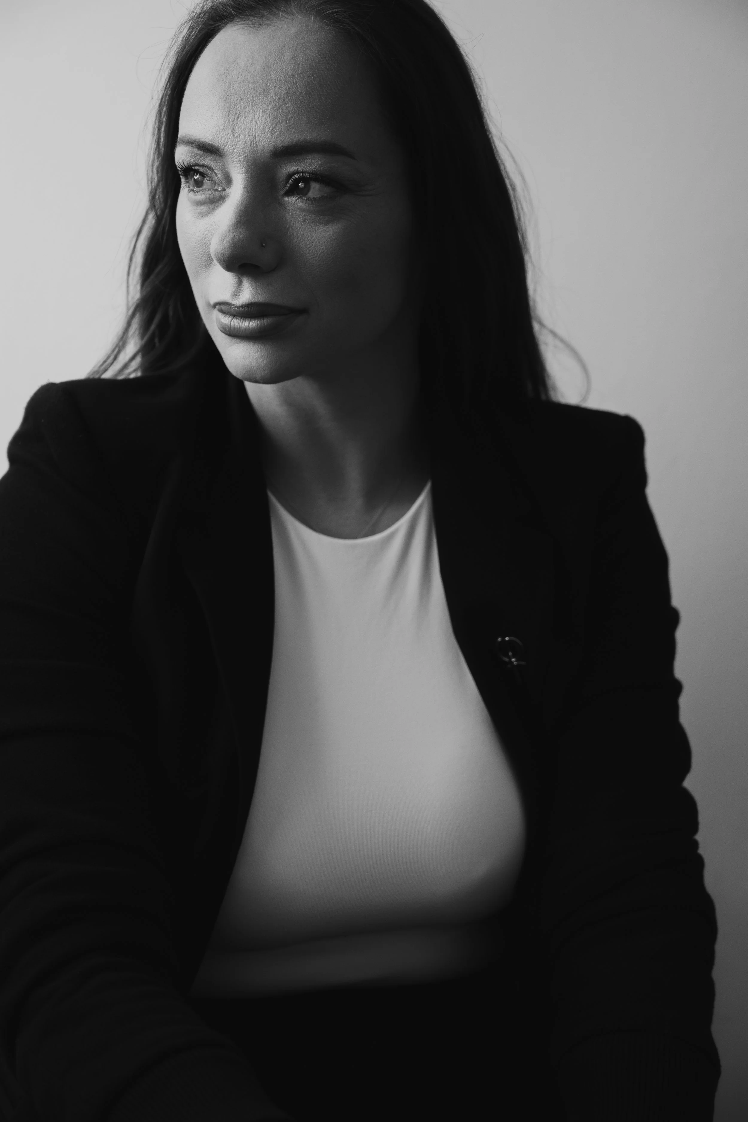 Black-and-white portrait of a woman with long dark hair, wearing a dark blazer and a white top, looking slightly to her left.