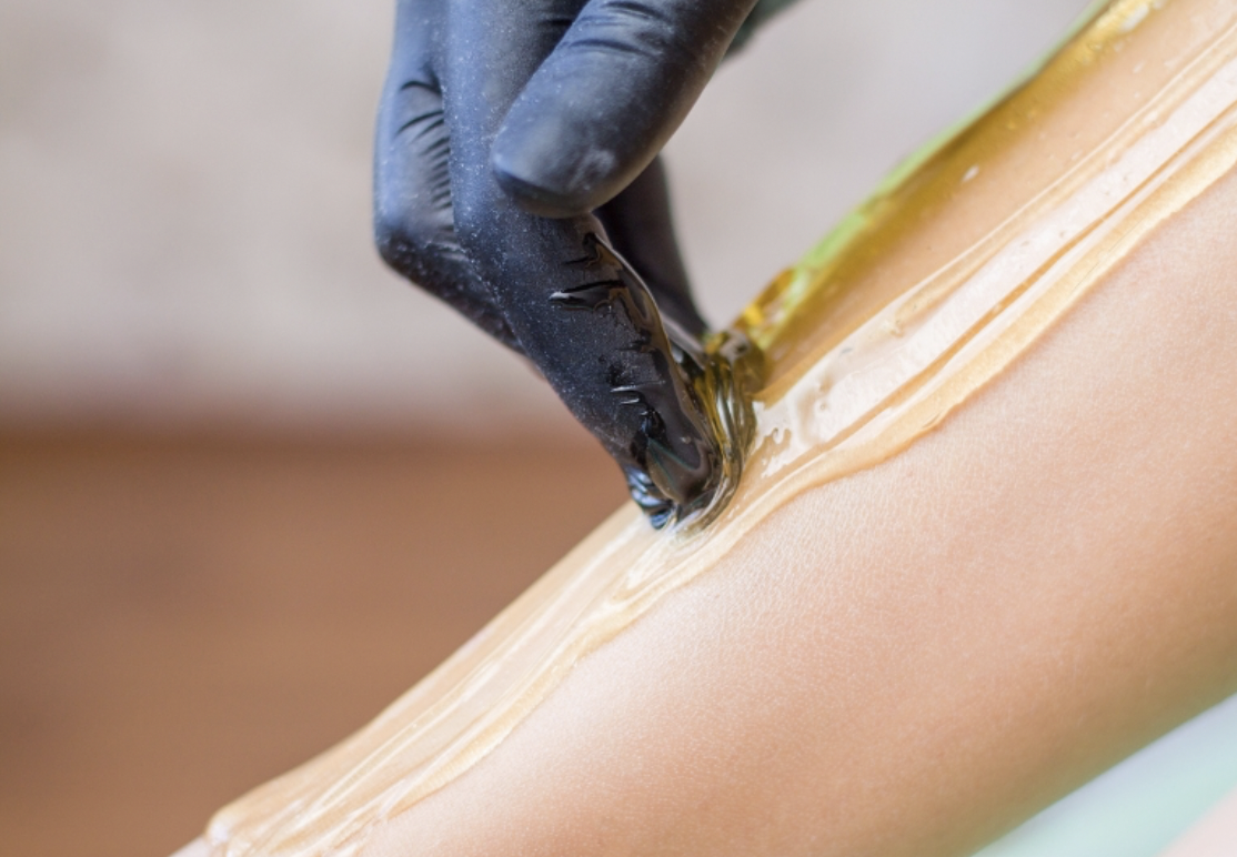 A person wearing black gloves applying wax strip for hair removal on their leg.