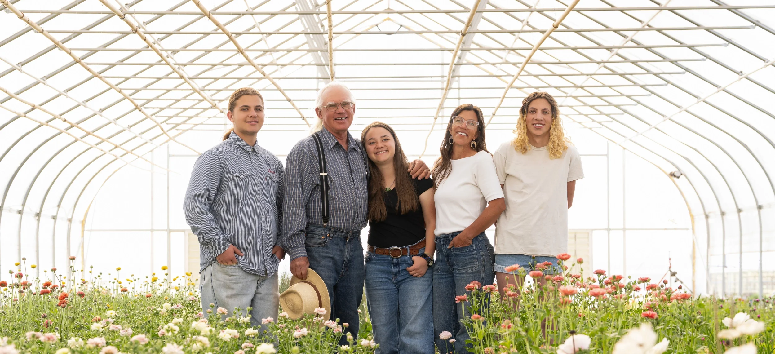 Whipstone Family portrait, five people standing in a green house with fresh flowers blooming.