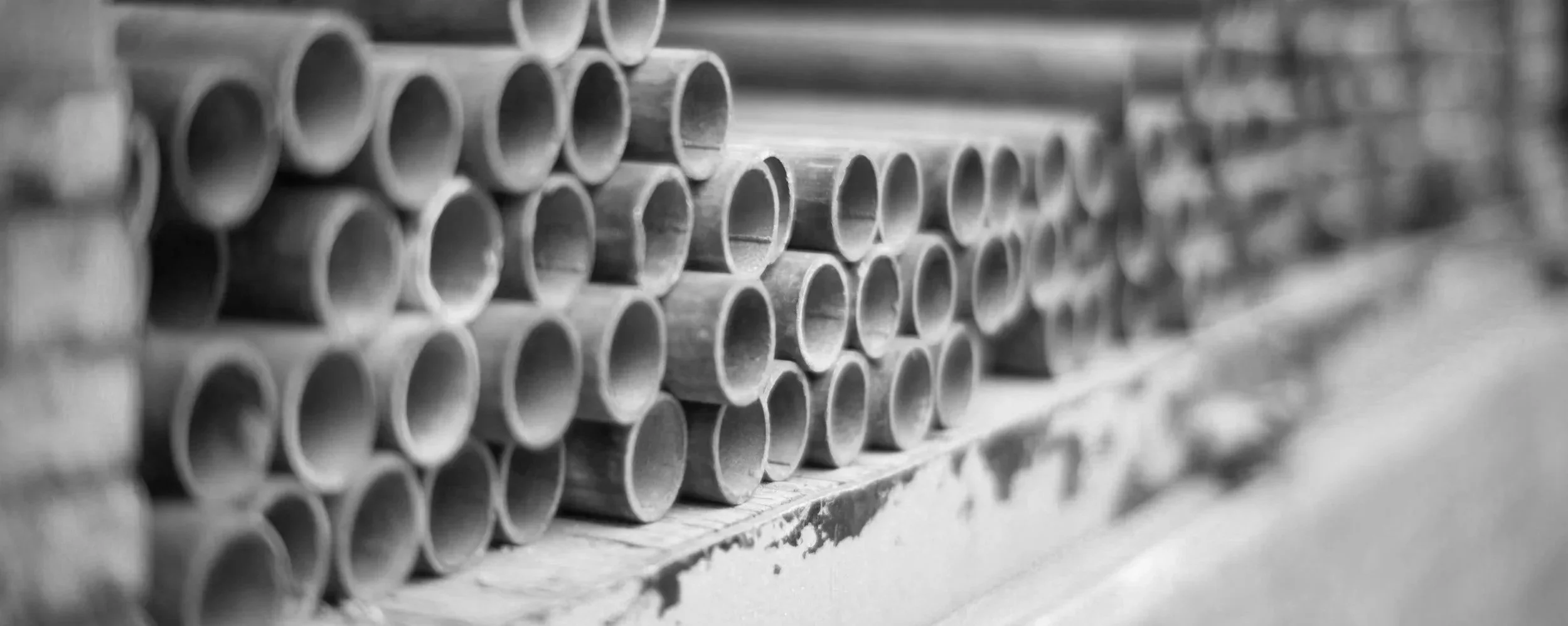 Black and white photo of stacked metal pipes likely in a warehouse or construction storage area.