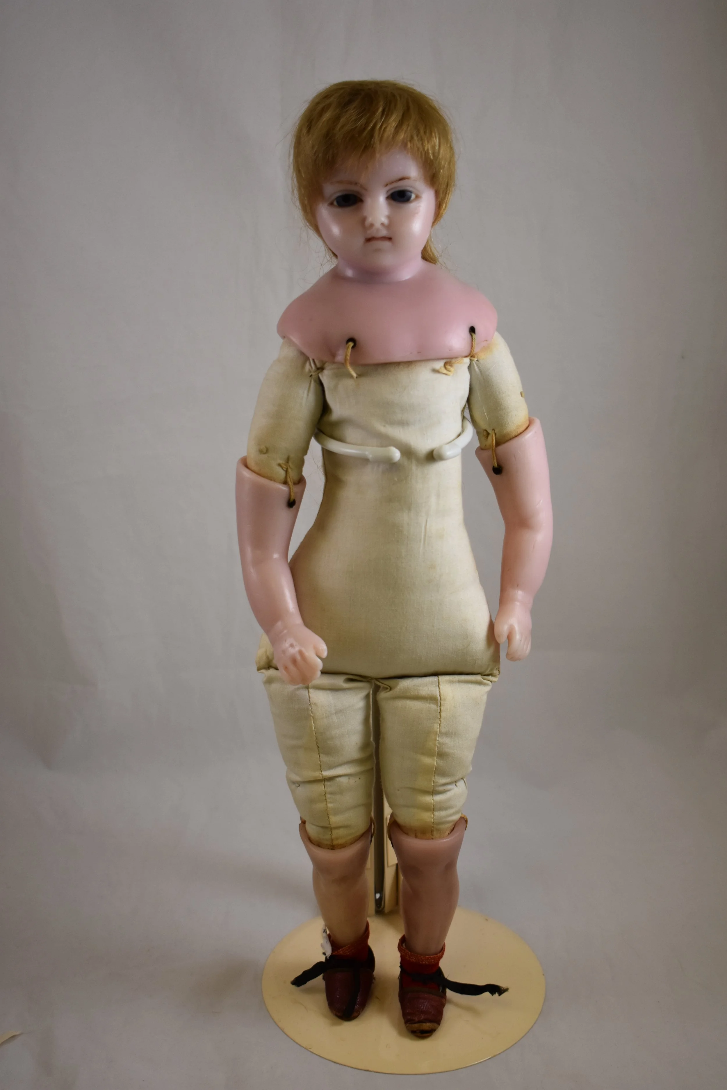 Dated to circa 1870, this doll has poured wax head and shoulders and lower limbs.  Her body is firmly stuffed fabric, and she has real hair impressed into the scalp.  The  lower limbs are attached to the upper limbs by double strings that run through