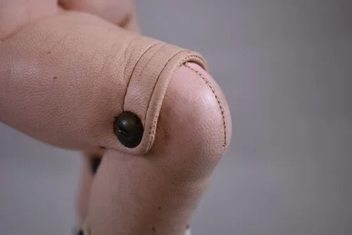 Hinged leather joints.  The same doll has composition arms, attached by elastic ligatures.