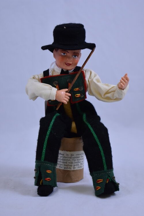 A Hilda S. Ege doll, Norwegian Setesdal Boy fiddler, wearing the traditional costume of the Setesdal region of Norway, showing local wisdom in the statement "The bigger the patch, the richer the man"