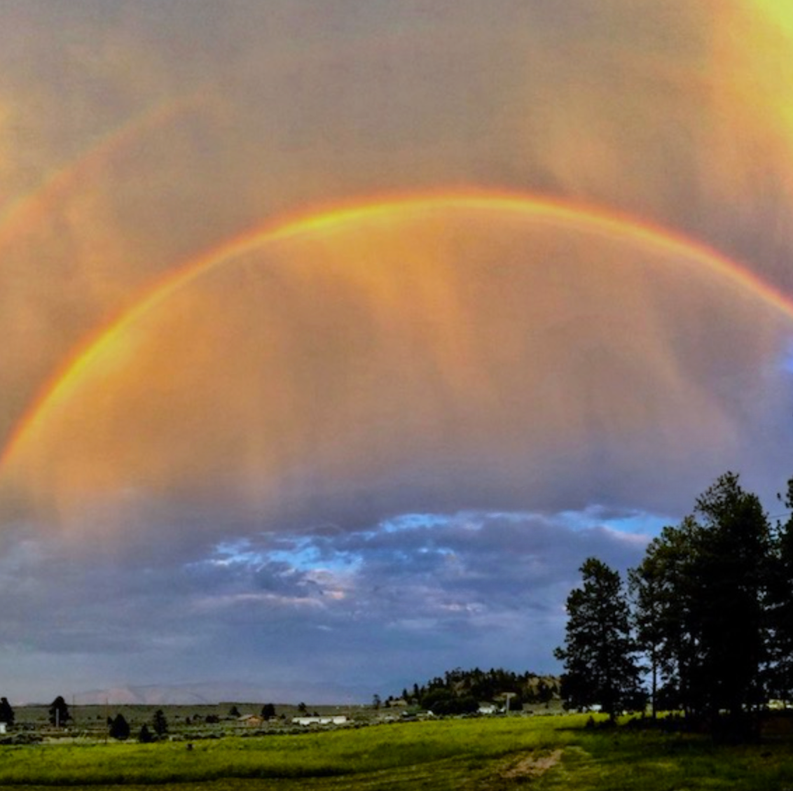 Rainbow over a landscape with trees and a cloudy sky.