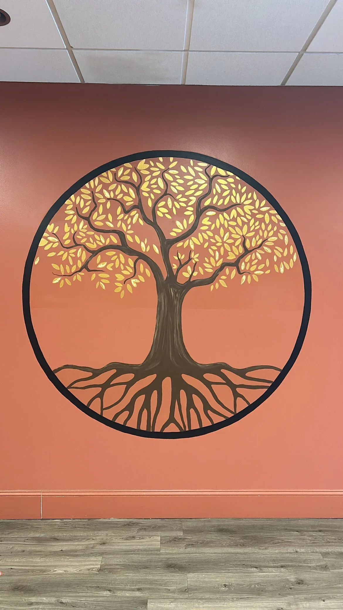 A painted mural of a tree with yellow leaves and detailed roots on a pink wall.