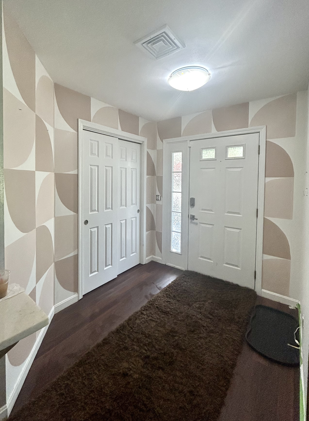 Entryway with patterned wallpaper, white door with window panels, brown rug, and a black doormat.