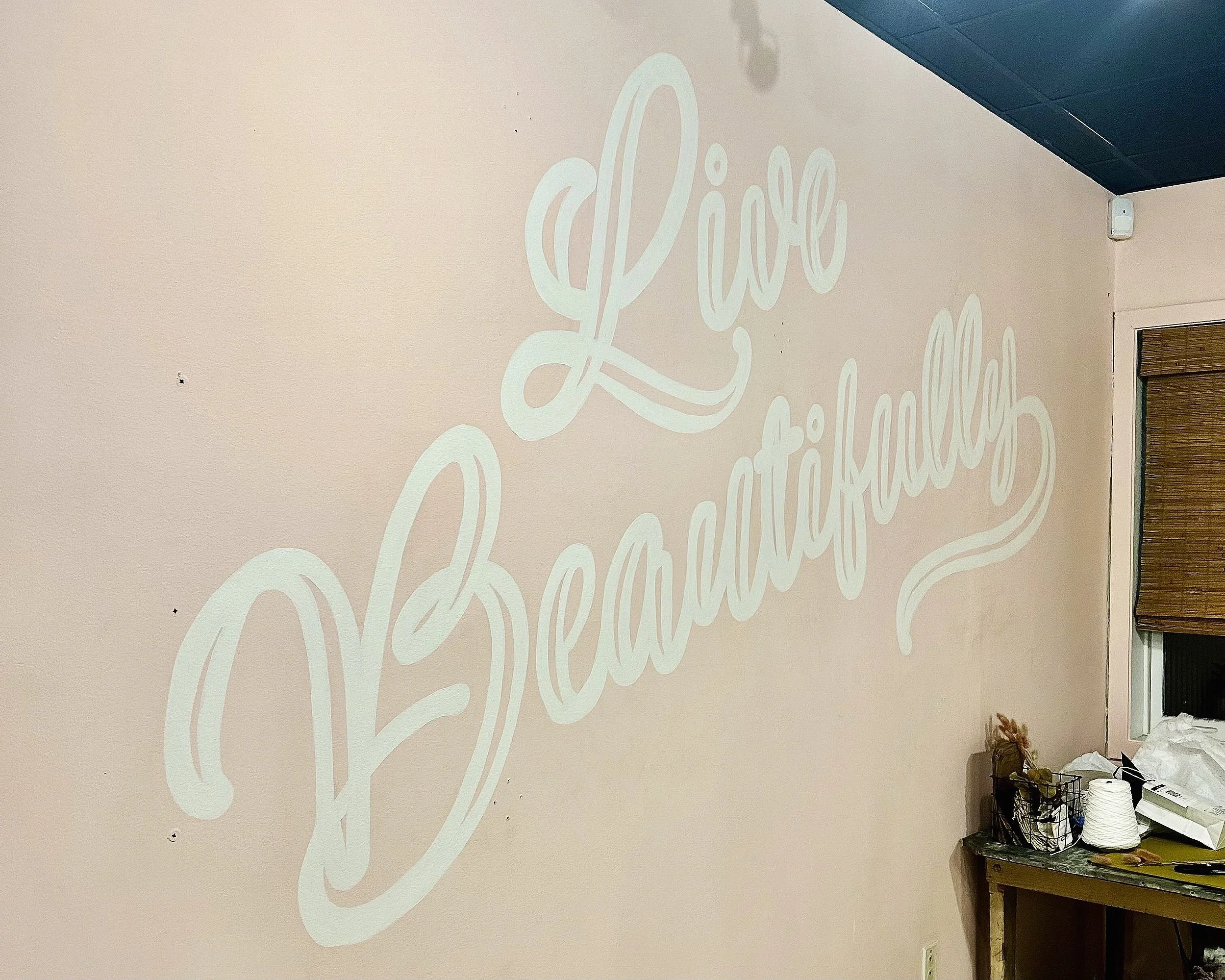 A wall with the phrase 'Live Beautifully' written in large, elegant cursive white letters.