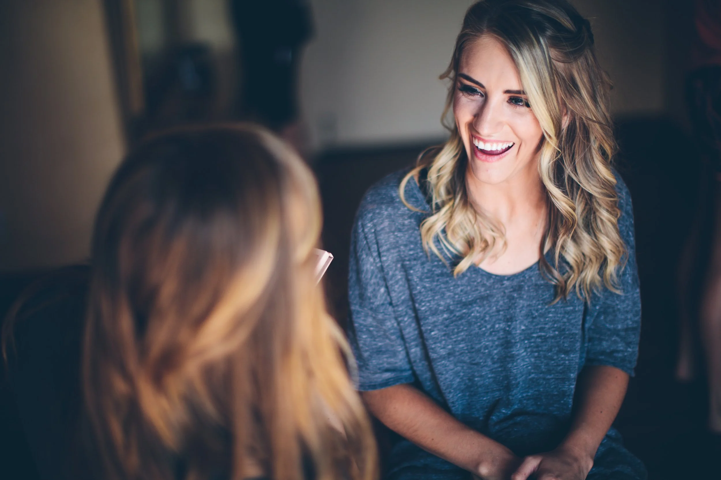 Two women engaged in conversation, smiling and enjoying each other's company indoors.