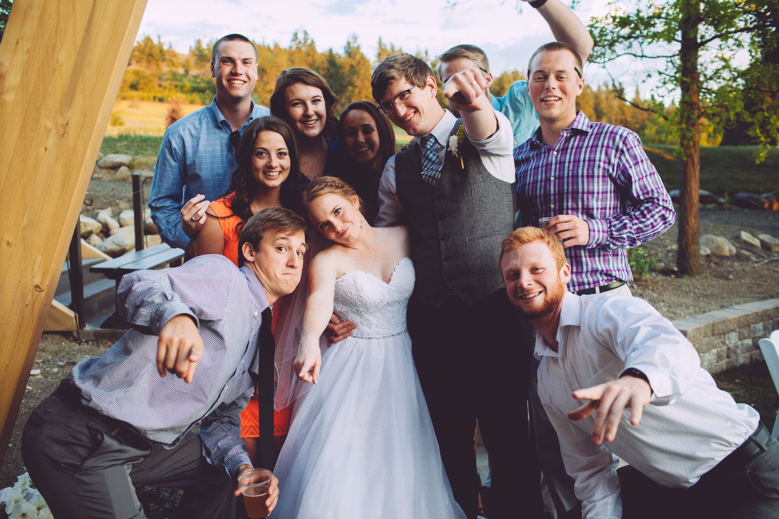 Group of people celebrating wedding outdoors with trees and a stone pond in the background.