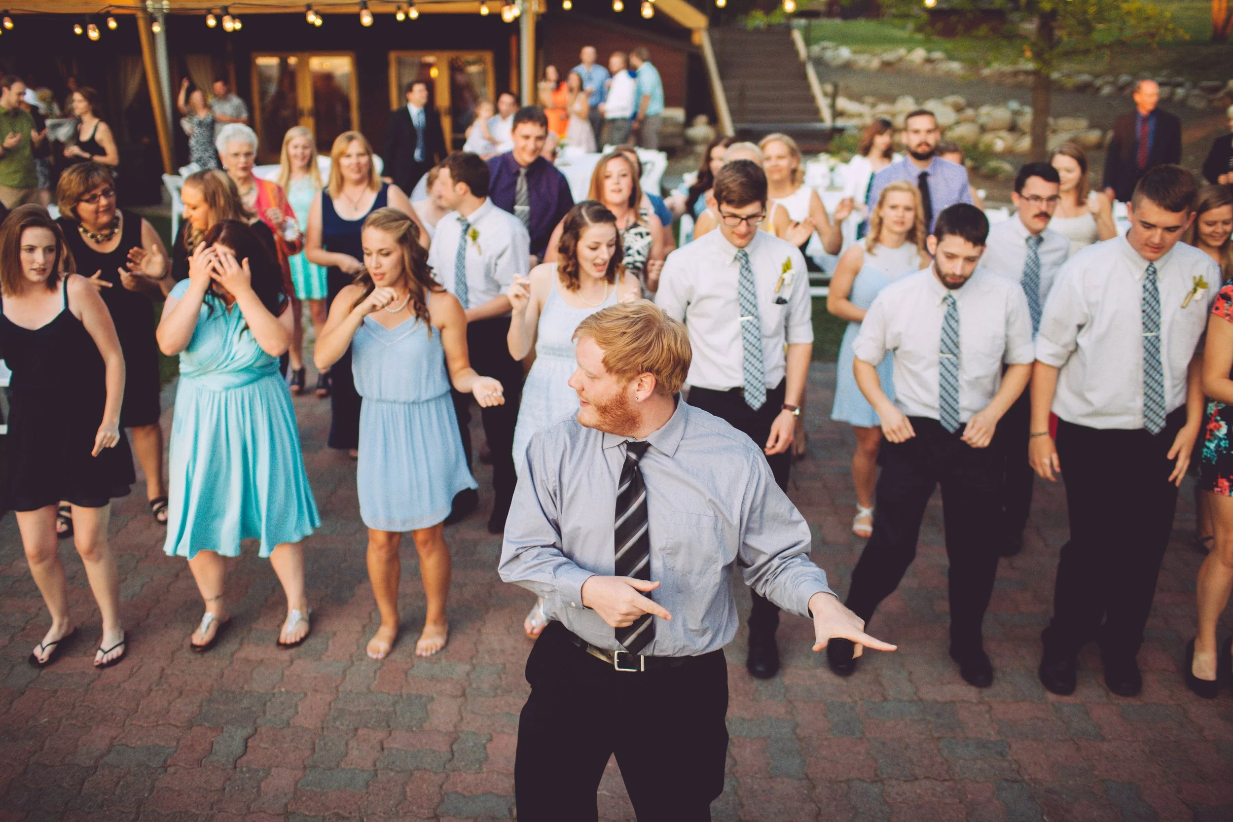 People dancing outdoors at a wedding reception or celebration, with a DJ or host leading the dance.