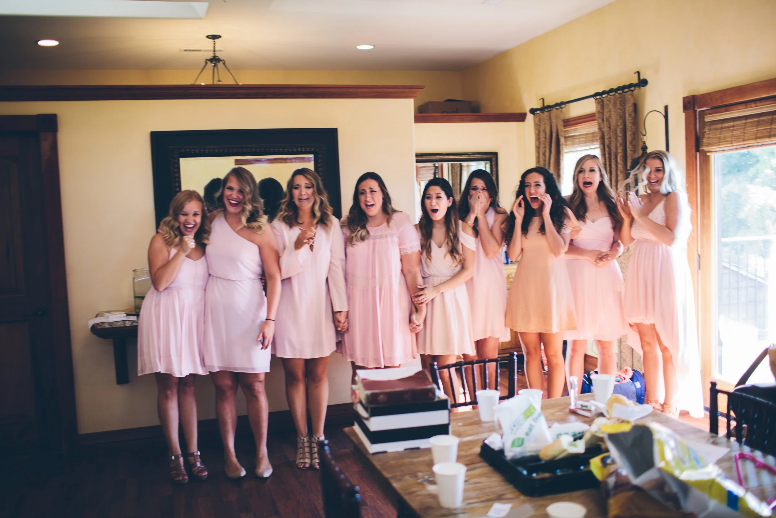 A group of ten women in pink dresses, standing indoors, visibly emotional and crying, possibly during a wedding or special event.