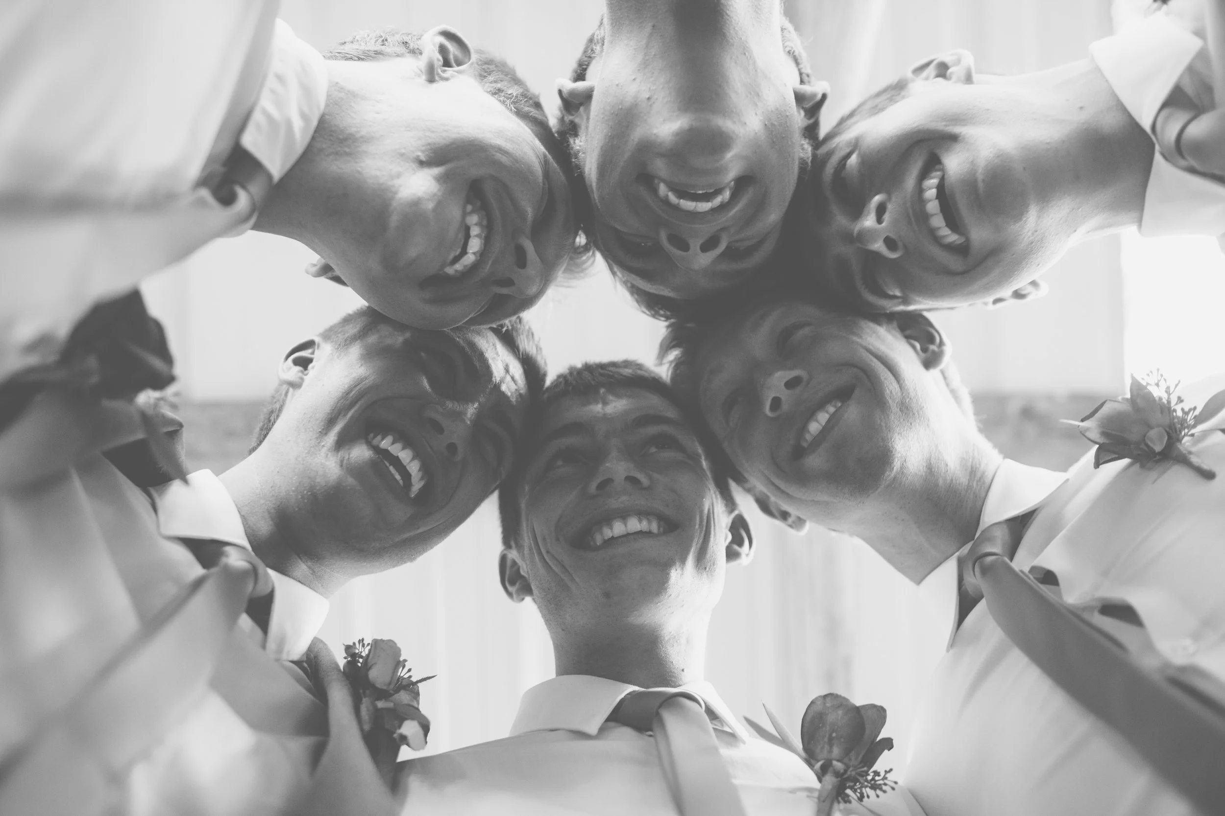 Group of six men in suits smiling and looking down at the camera, forming a circle.