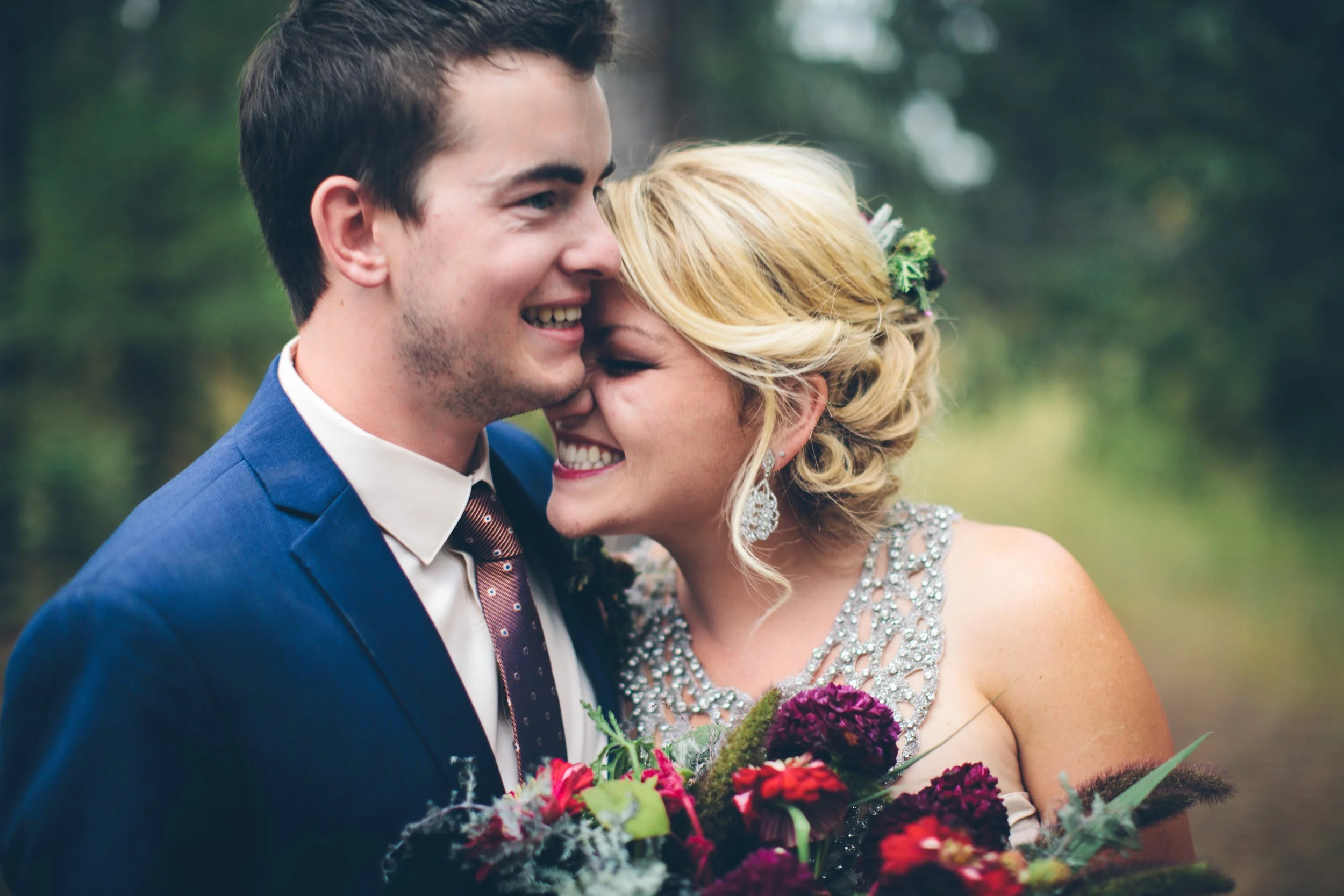 A smiling couple, dressed in wedding attire, sharing a joyful moment outdoors surrounded by greenery.