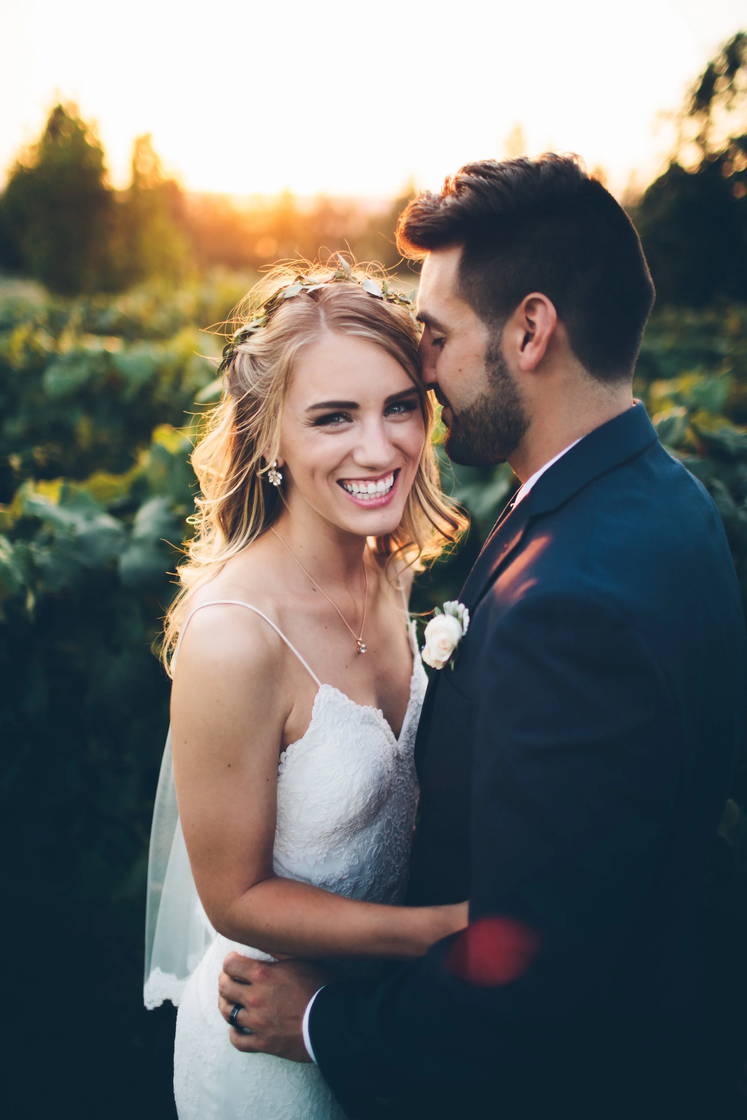 A smiling bride and groom in wedding attire celebrate outdoors at sunset.
