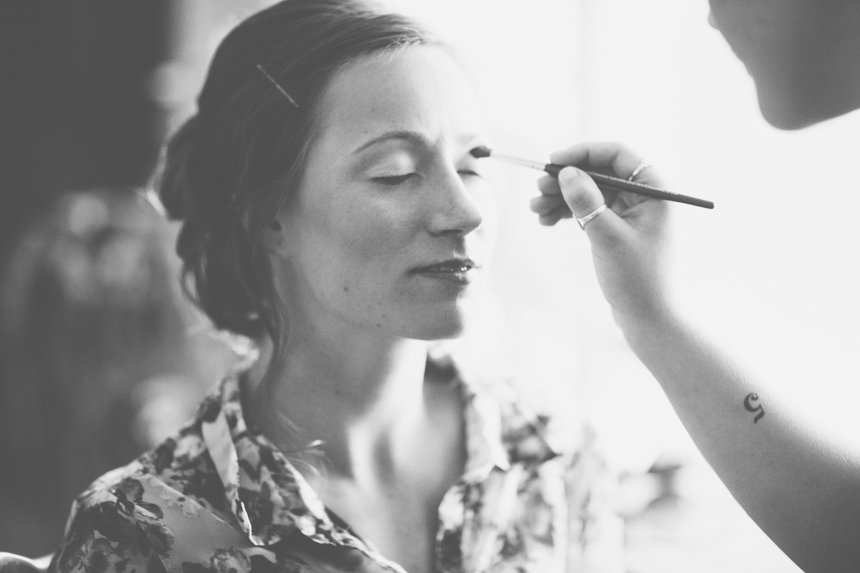 A woman with her eyes closed as a makeup artist applies makeup on her face.