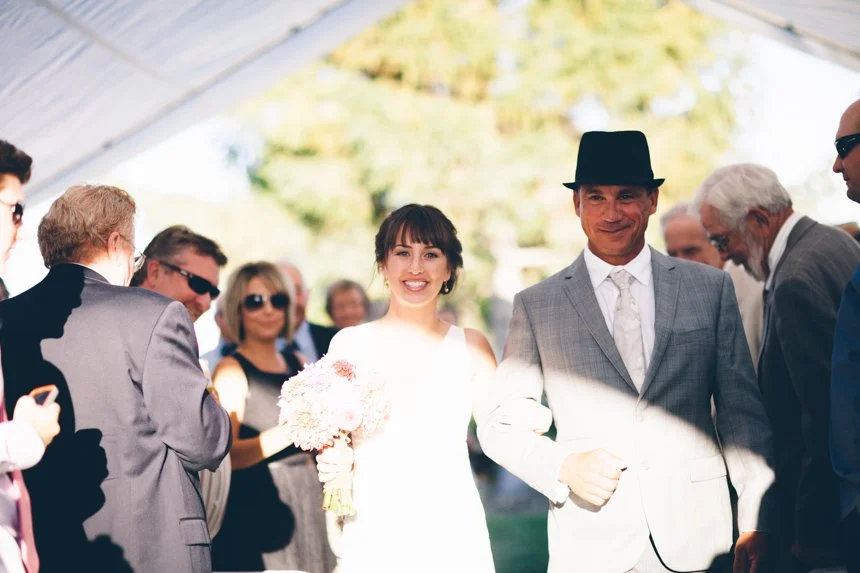 Bride and groom walking down the aisle at their wedding surrounded by guests under a tent.