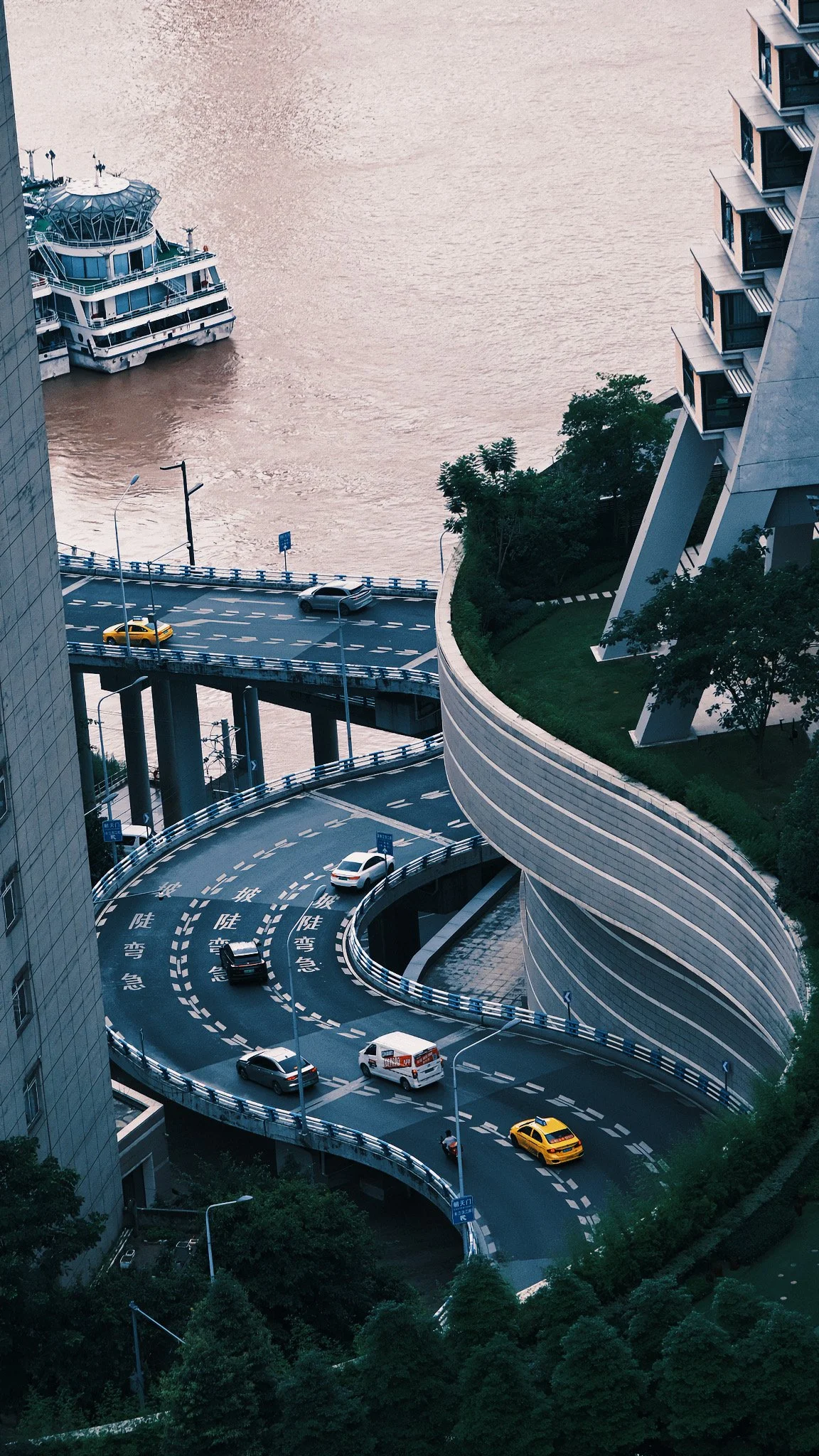 CHONGQING, CHINA — Cars navigate the curved elevated roadway near Raffles City in July 2024, overlooking the river and cityscape below.