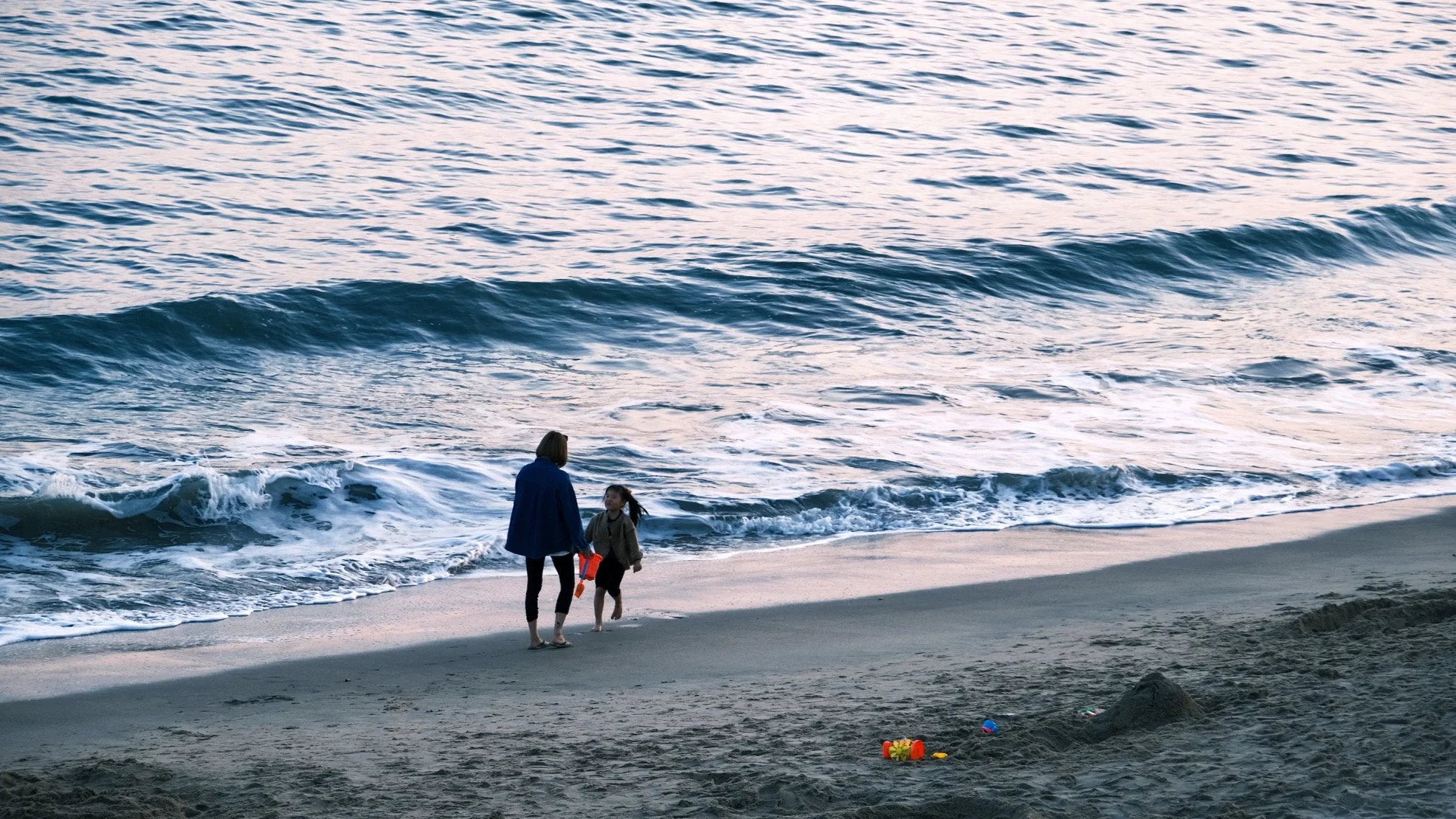 CHAOZHOU, CHINA — A parent and child walk
along the shoreline at sunset in January 2024, leaving footprints in the sand as waves roll in
along the coast.