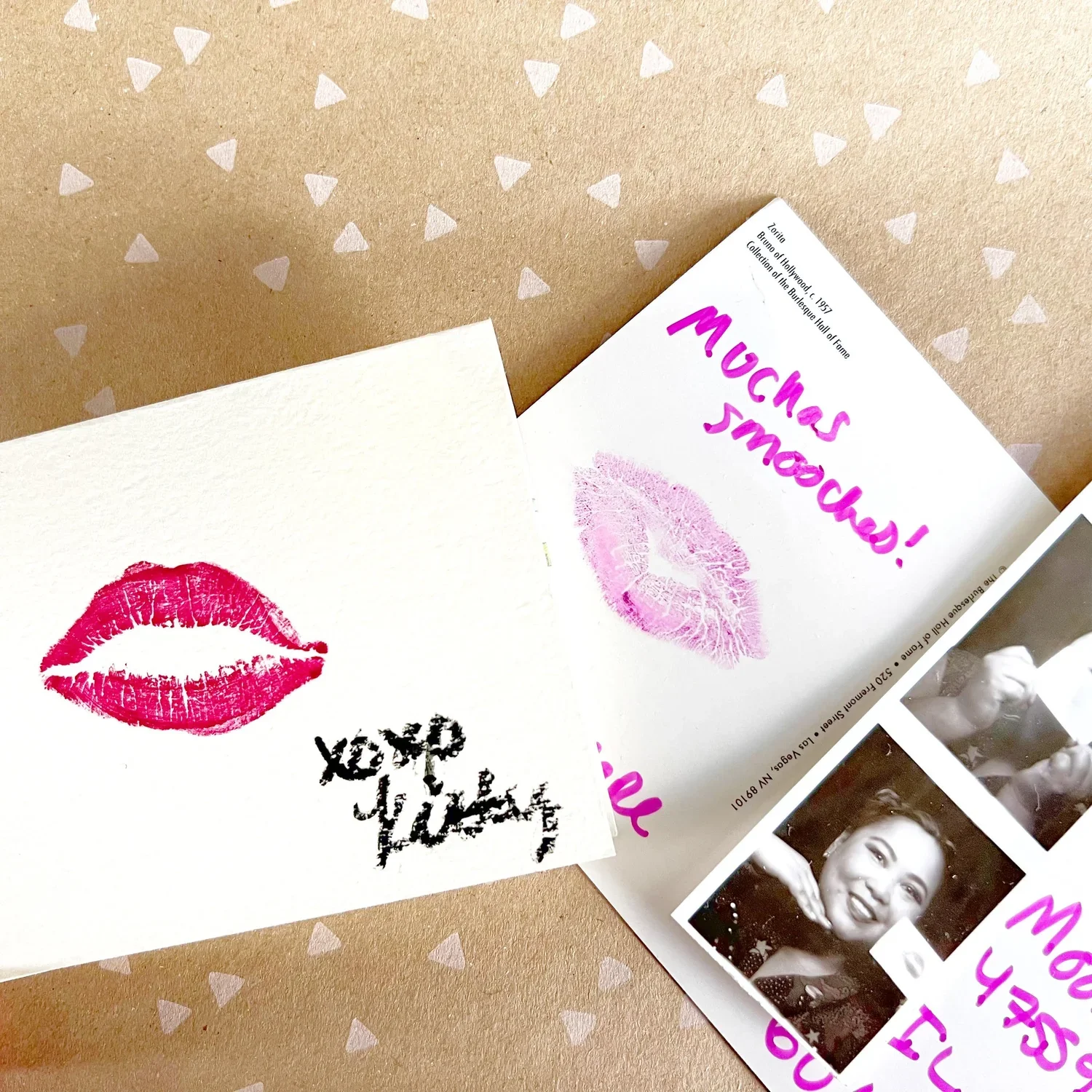 A greeting card with a red lipstick kiss mark and black text, partially visible, on white paper. Another paper features pink lipstick kiss marks and handwritten message in pink ink that says 'Muchas gracias!' on a white background with pink triangle patterns.