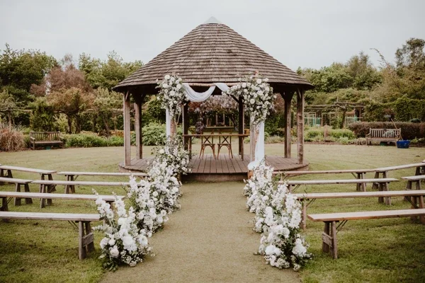 A decorated outdoor wedding gazebo with floral arrangements and benches for guests.