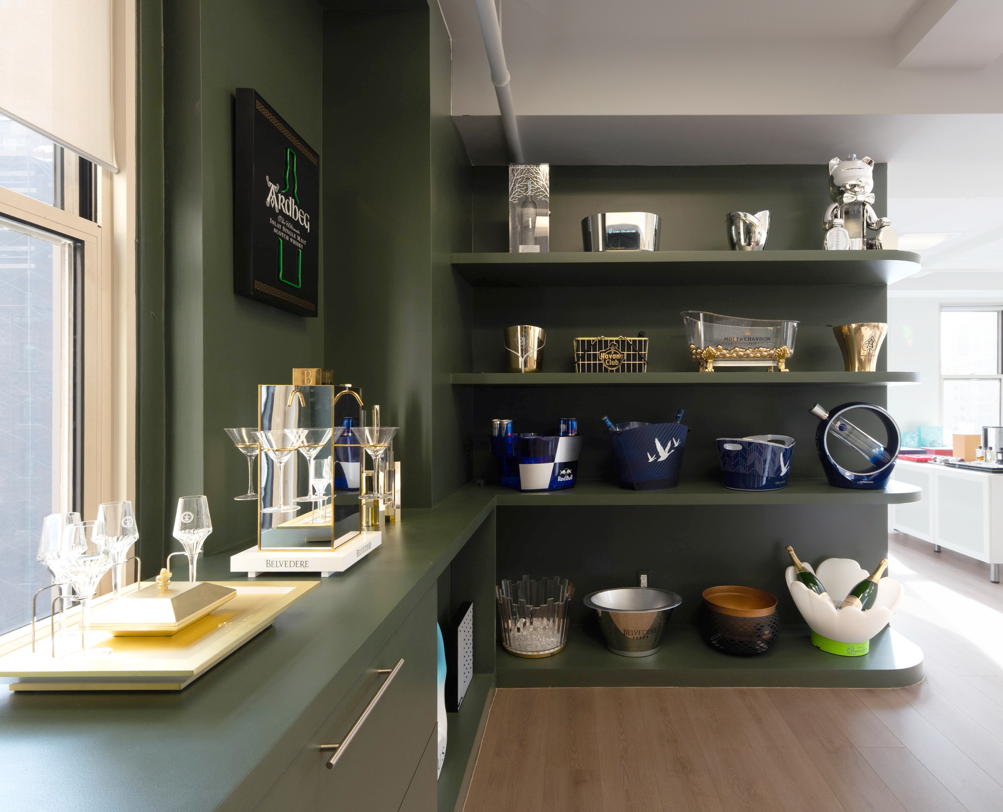 Display of various glassware and bottles on a green counter and shelves in a modern room