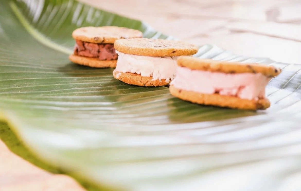 Three ice cream sandwiches with cookies and ice cream on a large green leaf.