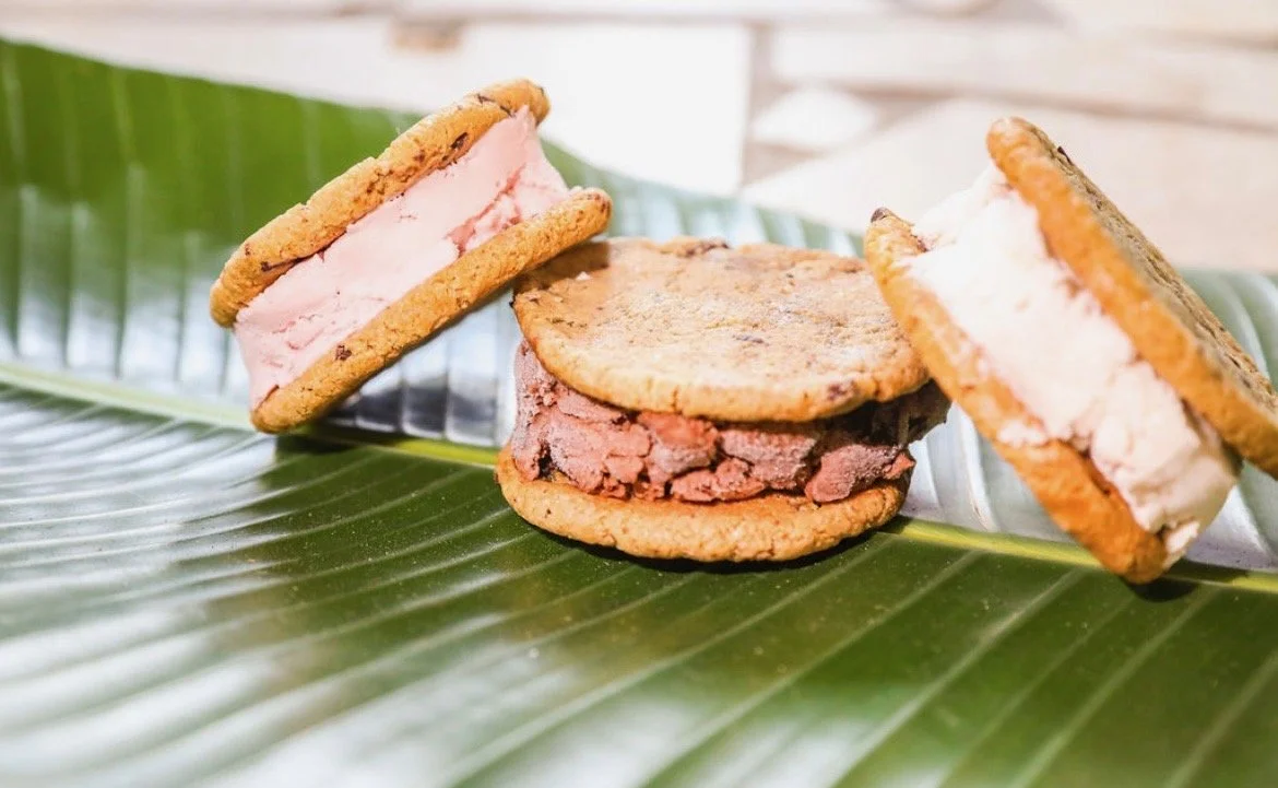 Three ice cream sandwiches with cookies and vanilla or chocolate ice cream on a green leaf.