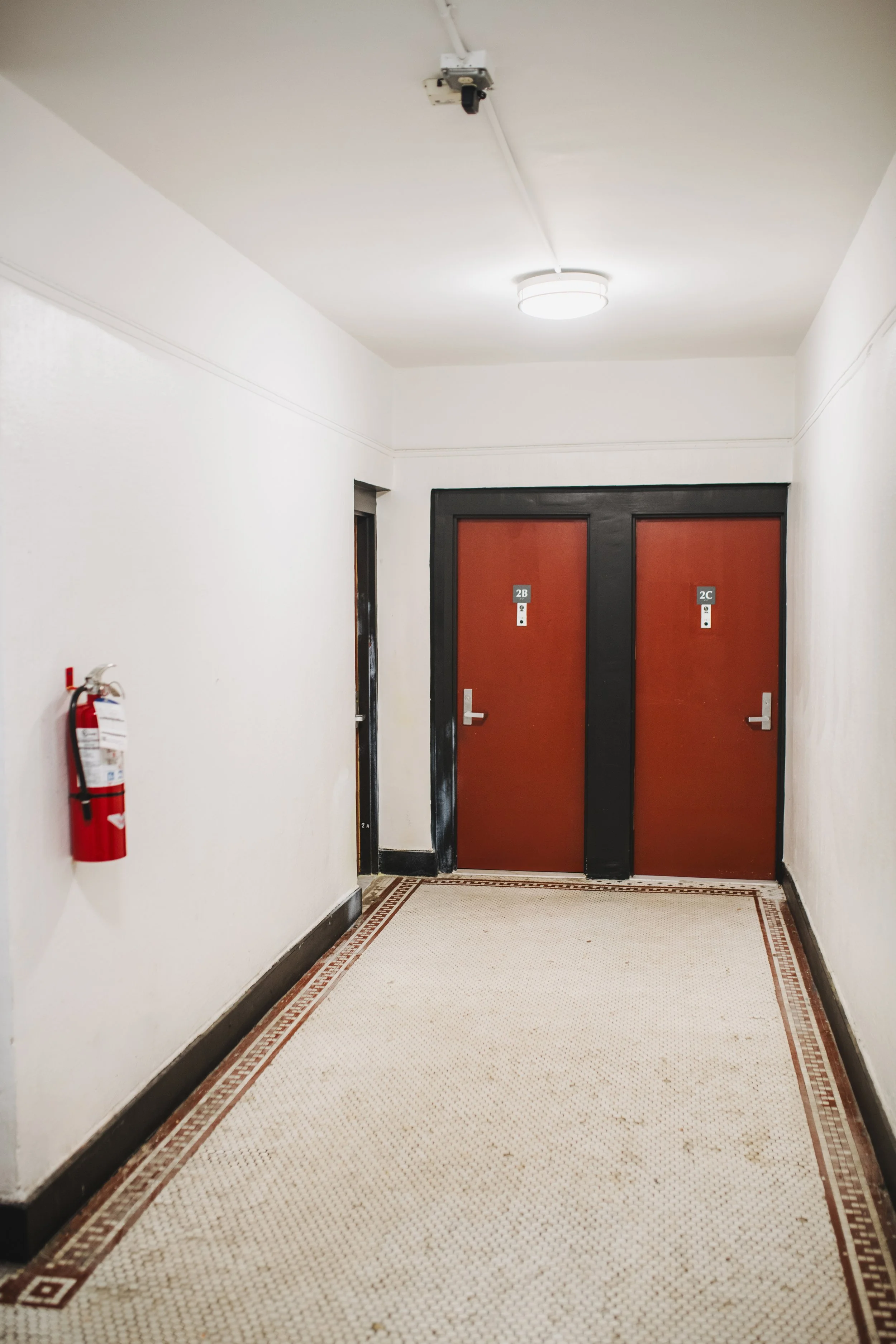 Hallway with white walls, a fire extinguisher on the left, a ceiling light, and two elevator doors labeled 2B and 2C.