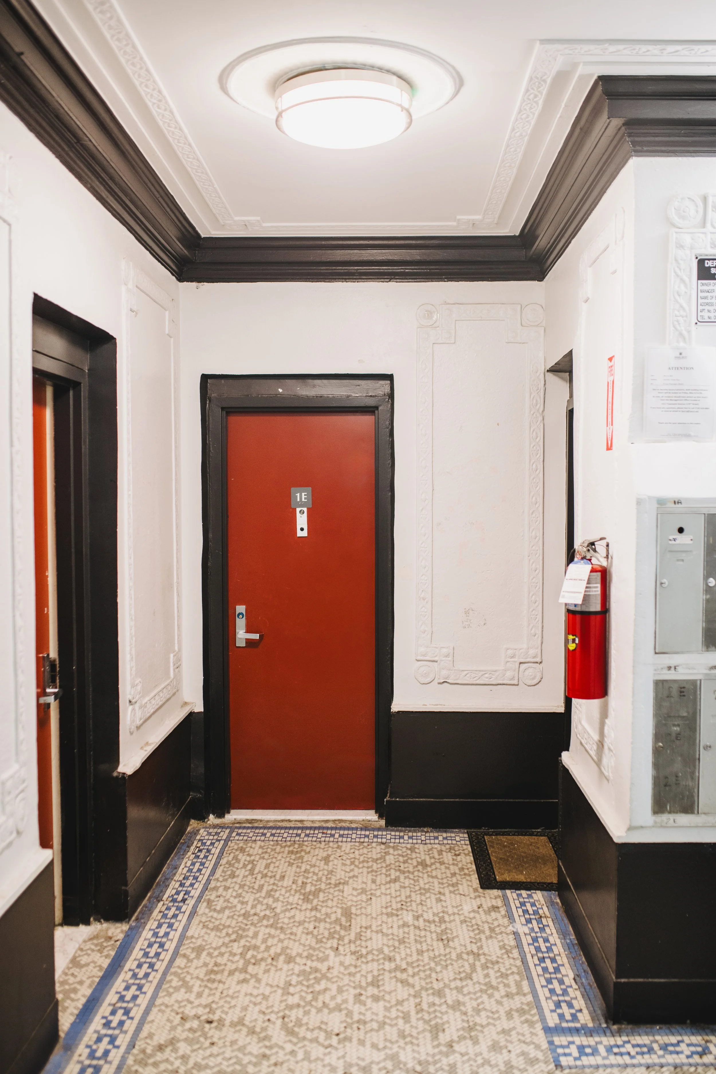 Interior hallway with ornate white walls, black crown molding, a patterned tile floor, and an elevator with a red door.