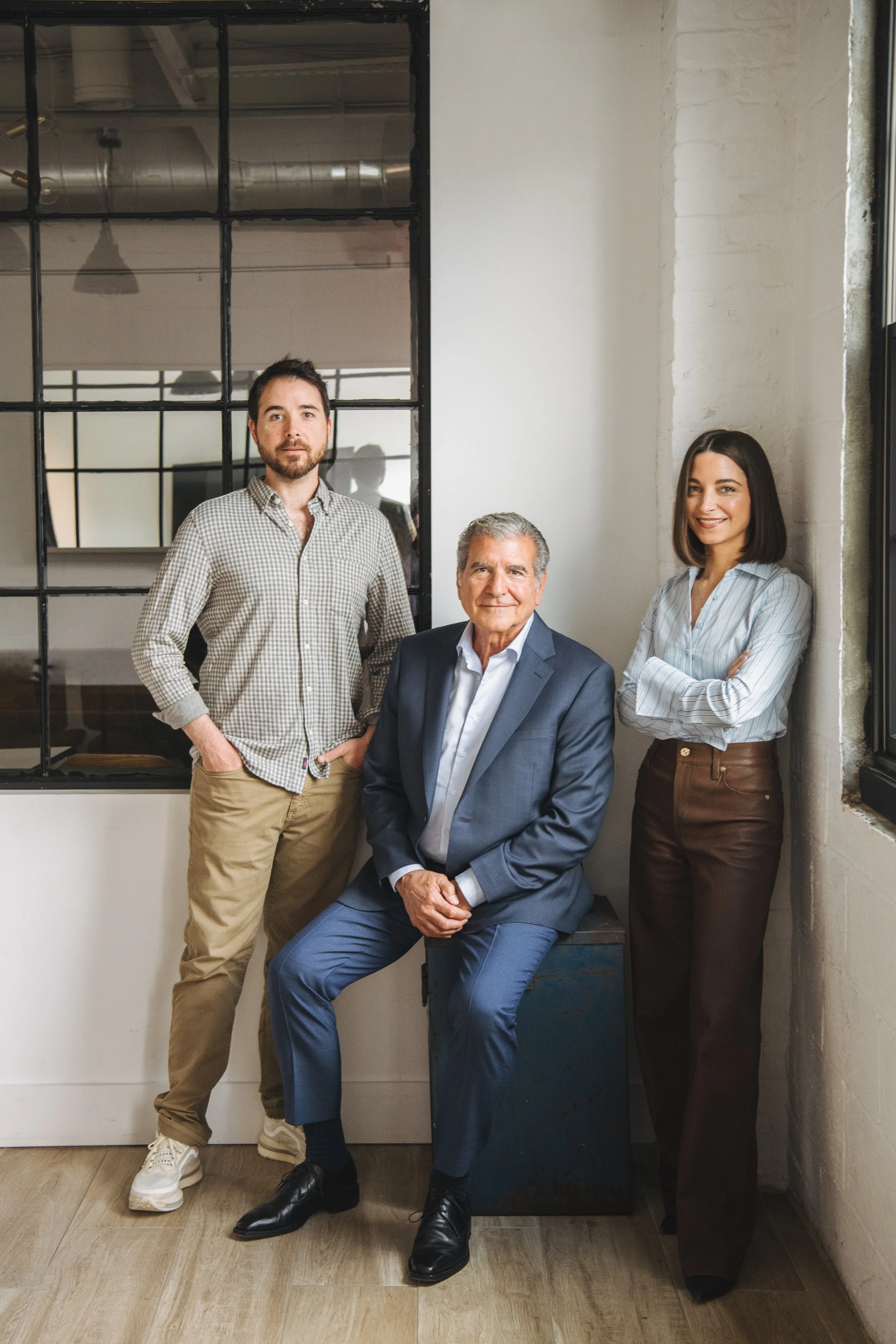 Four diverse business professionals posing in an office with white walls, a large window, and urban decor.
