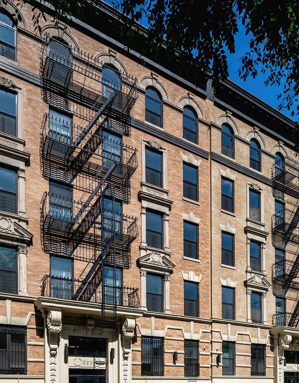 Historic brick apartment building with fire escapes on a sunny day.