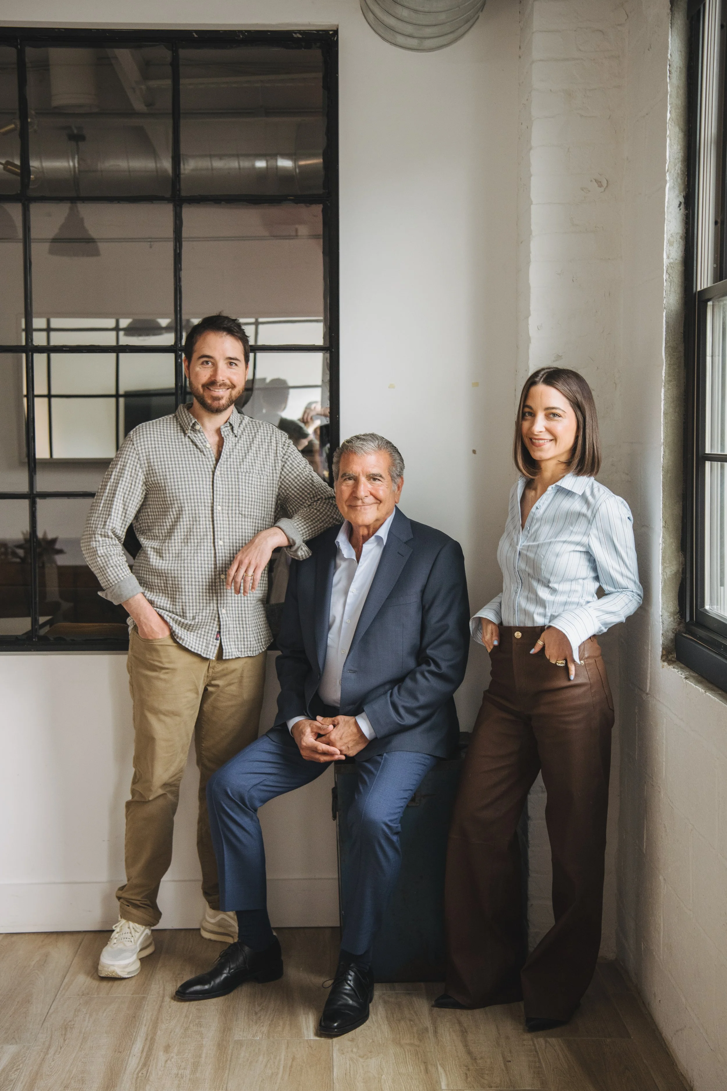 Four adults, two men and two women, posing together in a modern office with white brick walls and large windows, smiling at the camera.