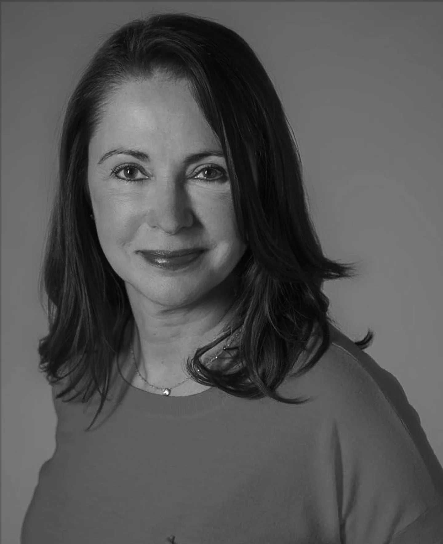 Black and white portrait of a woman with shoulder-length dark hair, wearing a top, smiling slightly, against a plain background.