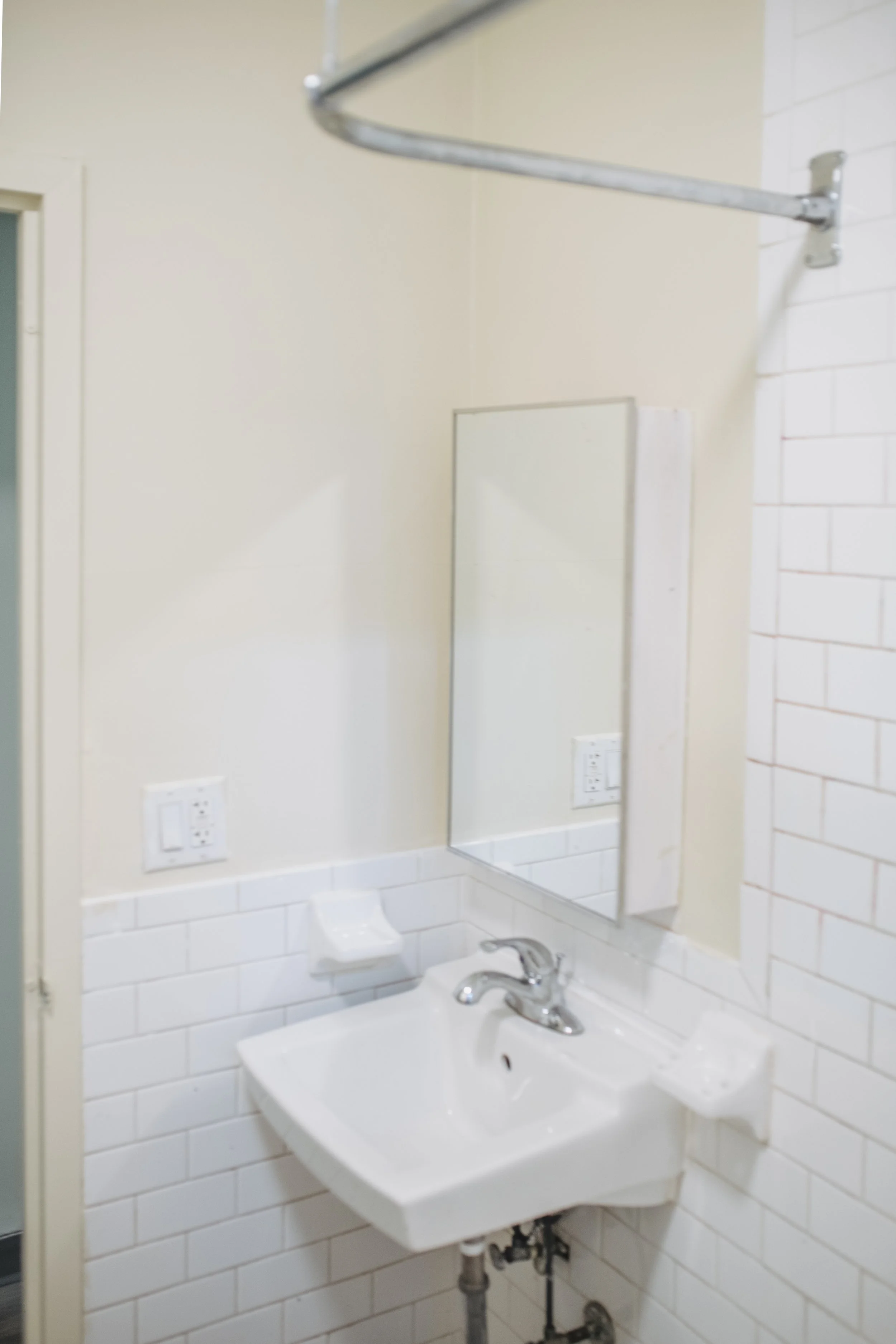 Small bathroom with a white sink, mirror, and tiled wall, featuring multiple electrical outlets.
