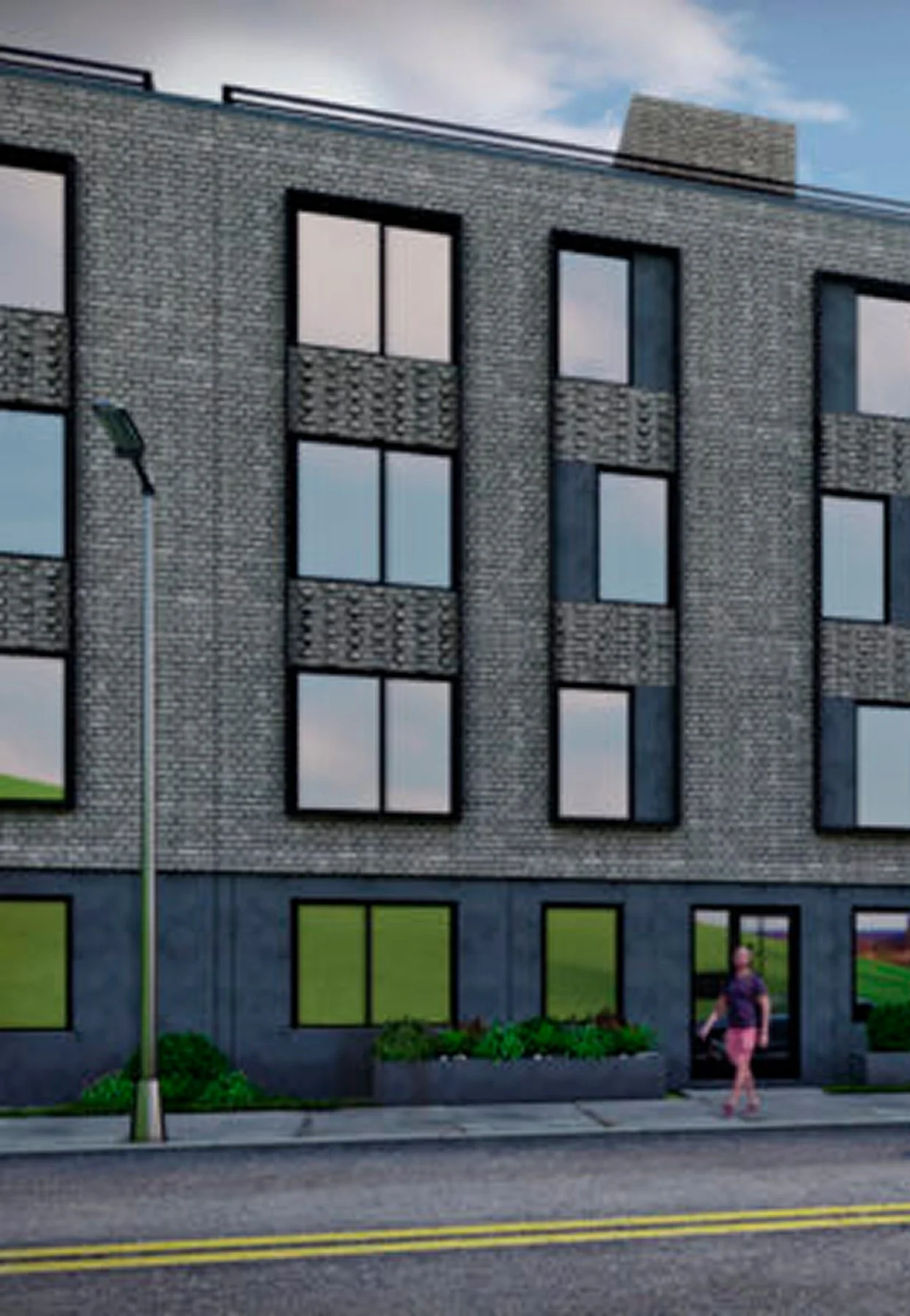 Modern brick apartment building with large windows, green lawn at the base, a person walking on the sidewalk, street with double yellow lines, and a streetlamp in front.