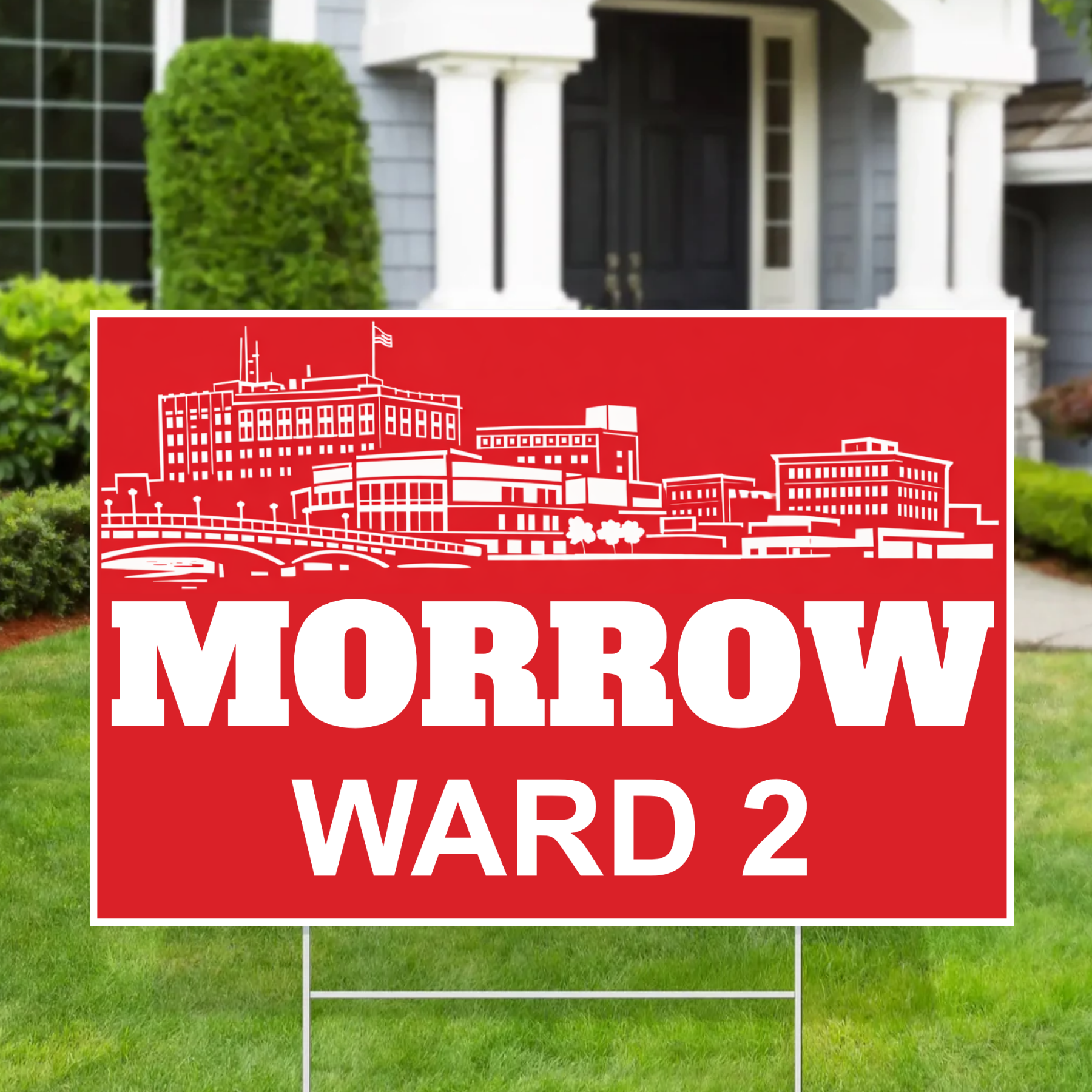 A red yard sign with a white illustrated skyline and the text 'MORROW WARD 2' placed in a front yard of a house.