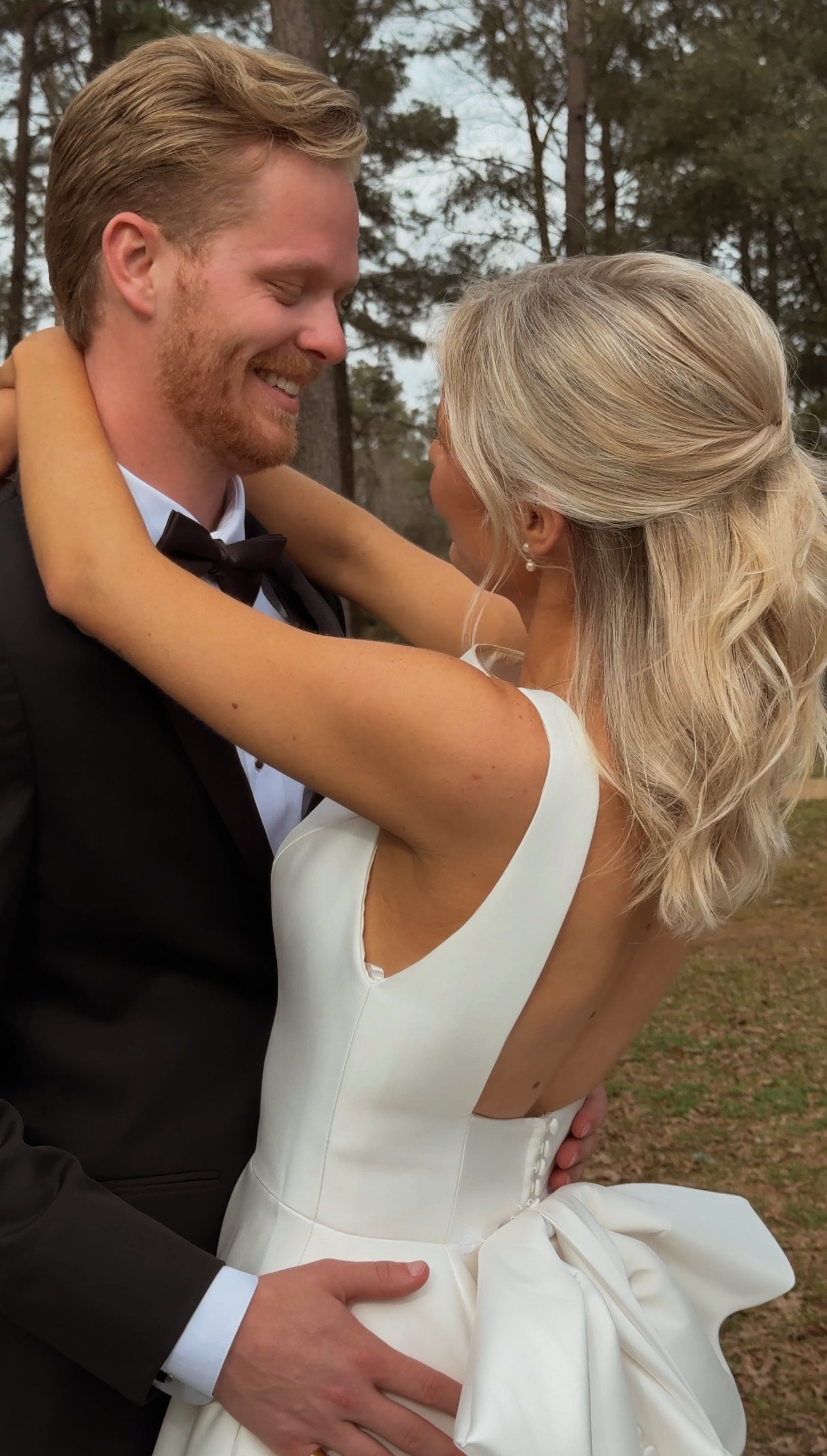 A couple on their wedding day, with the bride wearing a white dress with a bow at the back and the groom in a black tuxedo, smiling at each other. Wedding Content Creator, Louisiana Wedding Content Creator, New Orleans Wedding Content Creator,